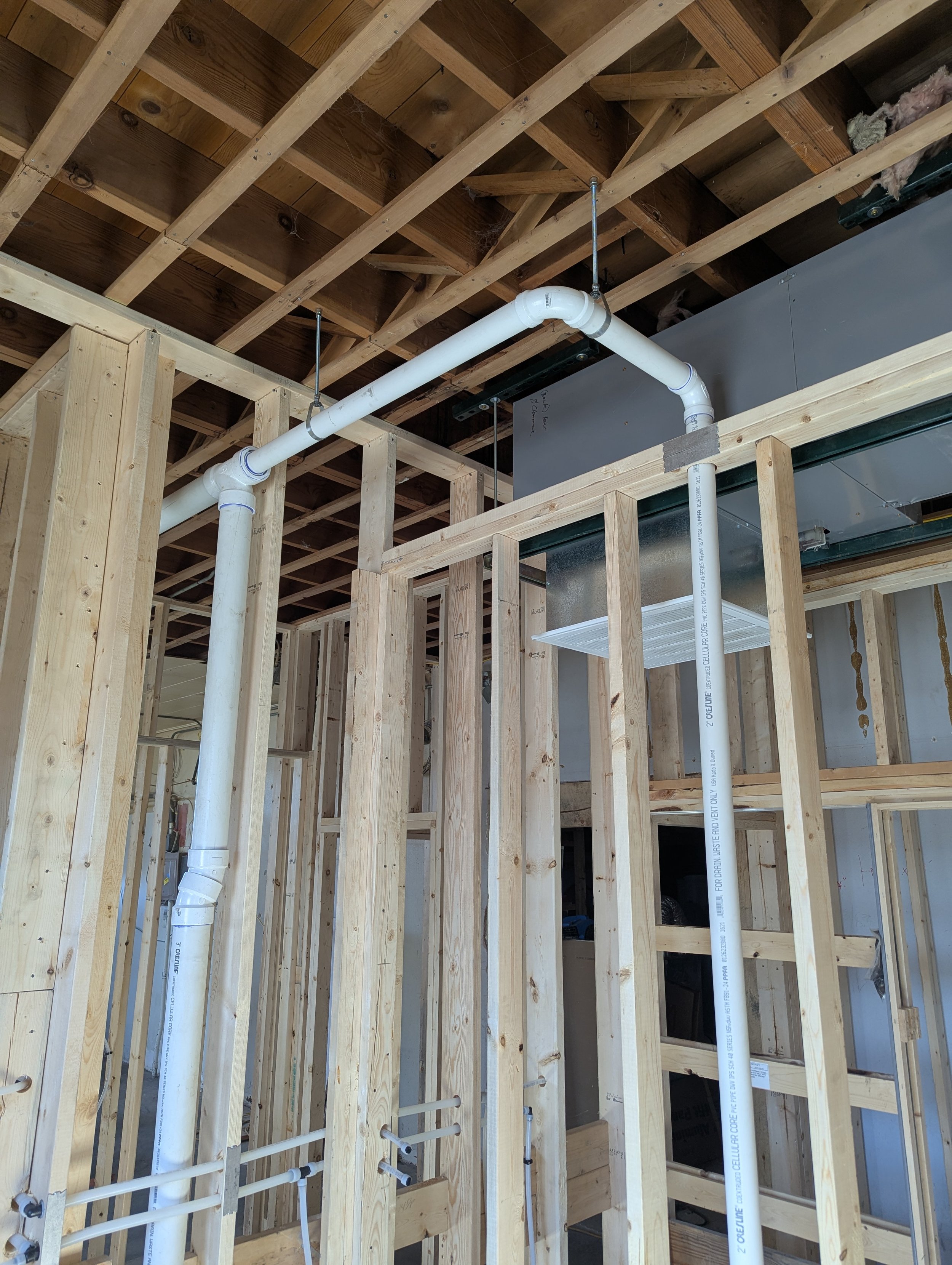 Construction site with exposed wooden framing and white PVC pipes installed for plumbing.