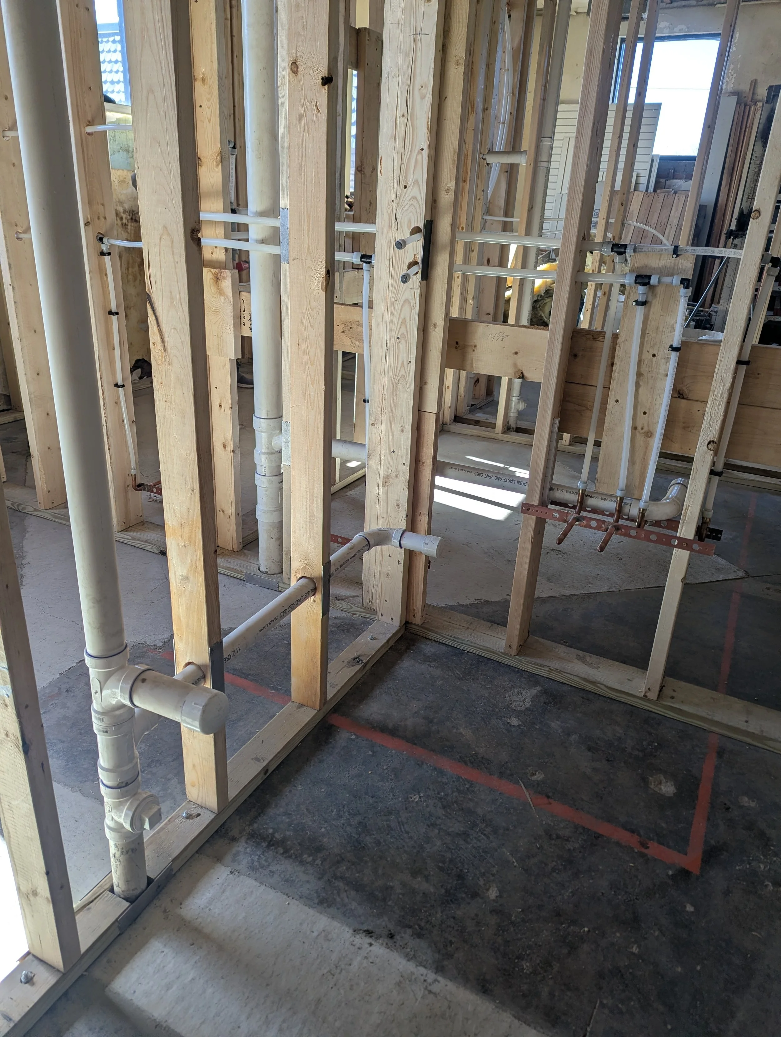Interior of a building under construction with exposed wooden framing and plumbing pipes.