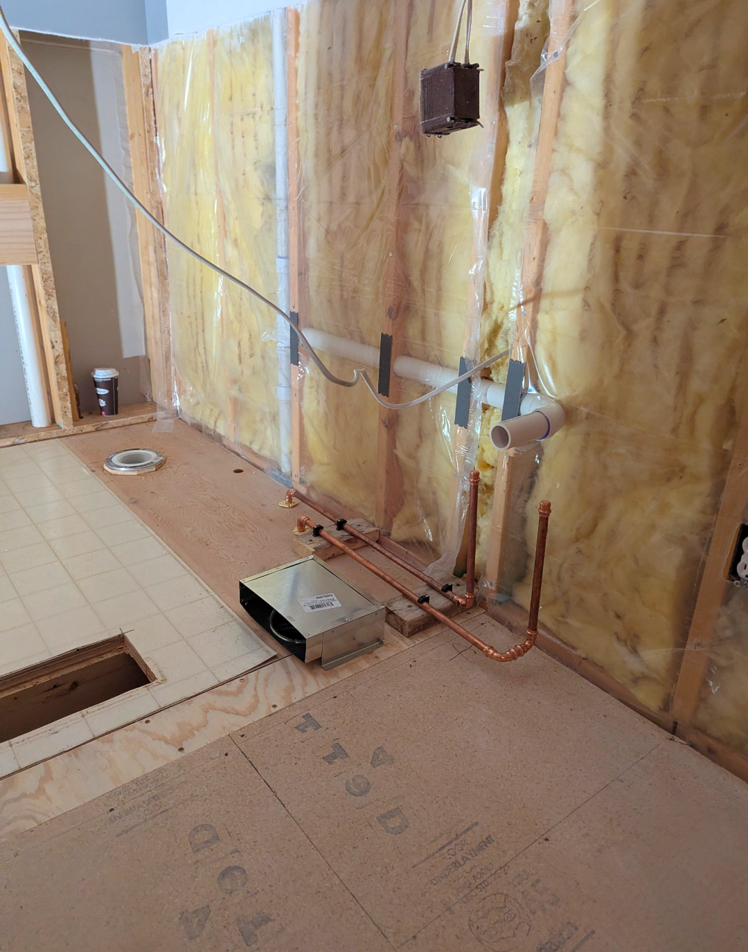Construction site with plumbing pipes, copper fittings, and insulation in a room under renovation.
