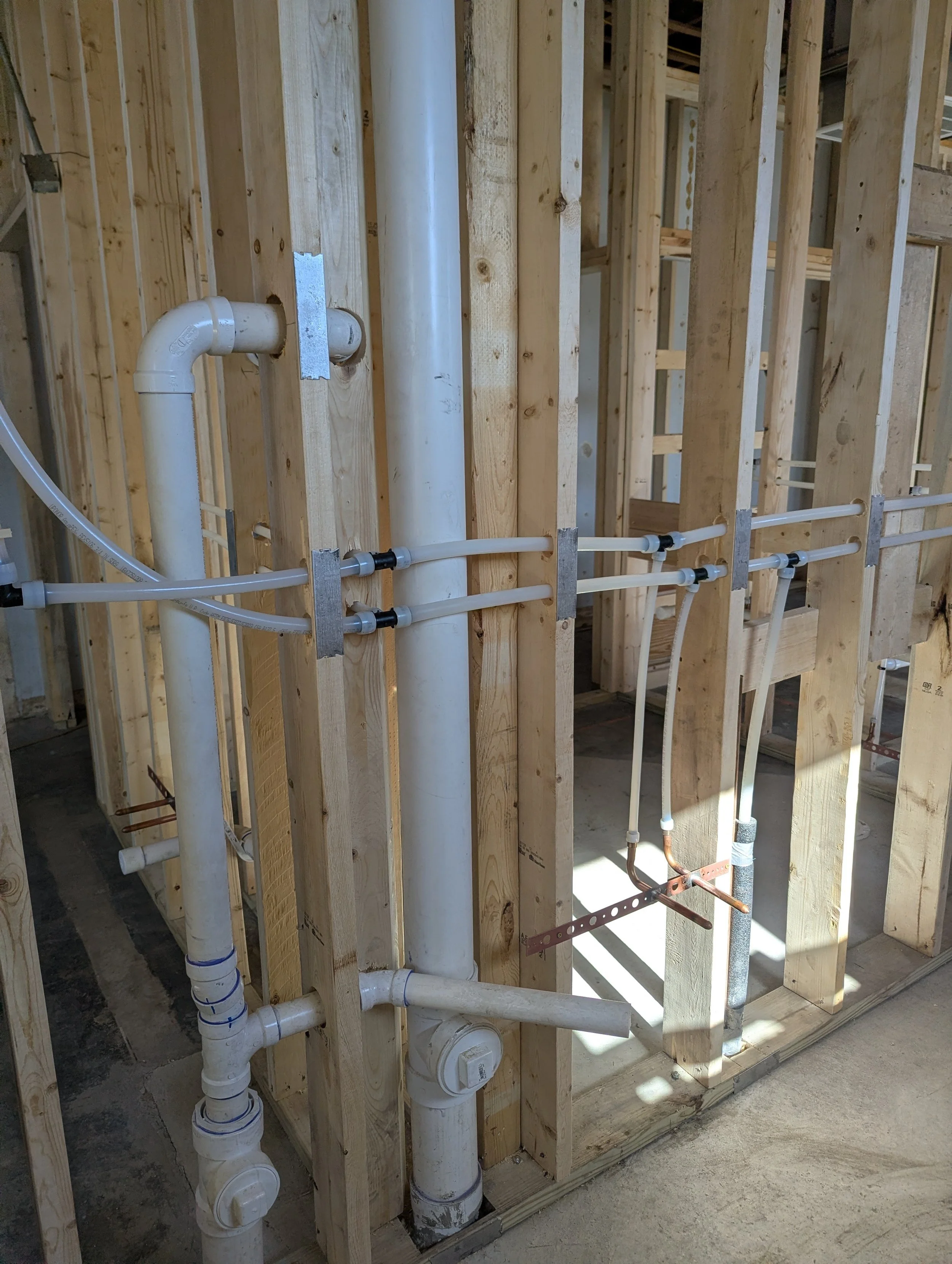Plumbing pipes and fixtures installed within a wooden framing of a building under construction.