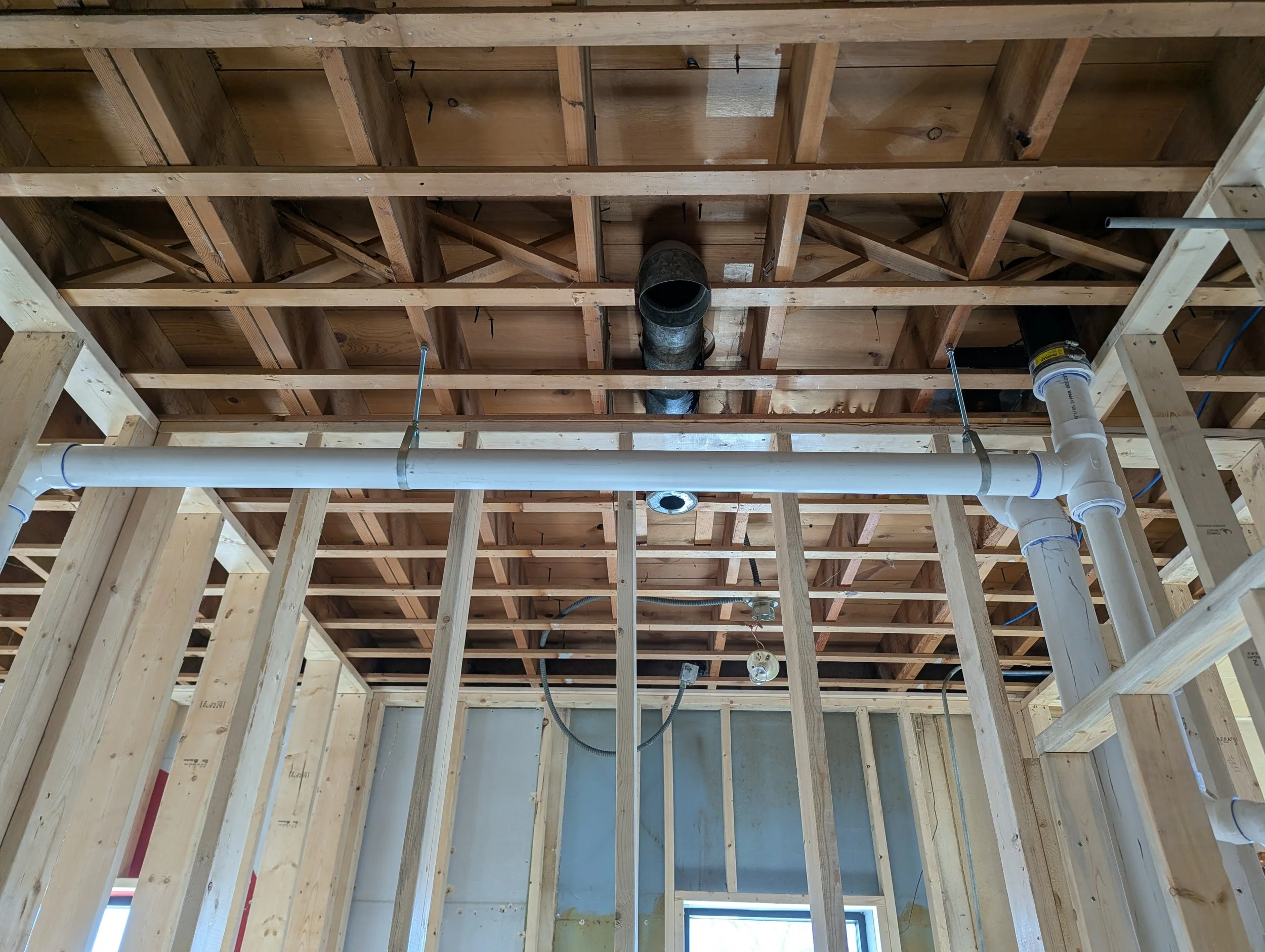 Construction framing with wooden studs and plumbing pipes installed in a building under construction.