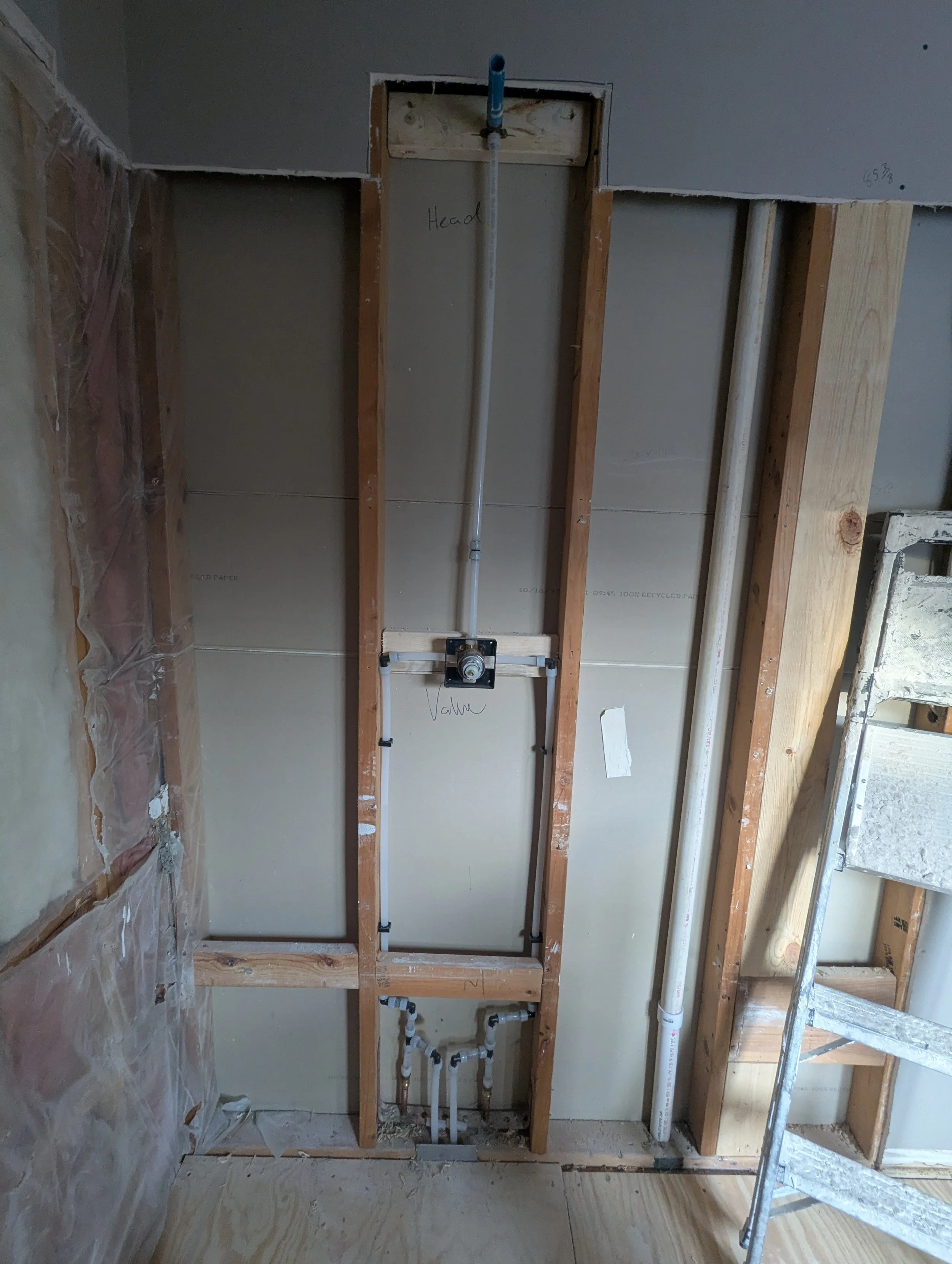 Open wall with plumbing pipes and electrical wiring, construction site with scaffolding on the right side.