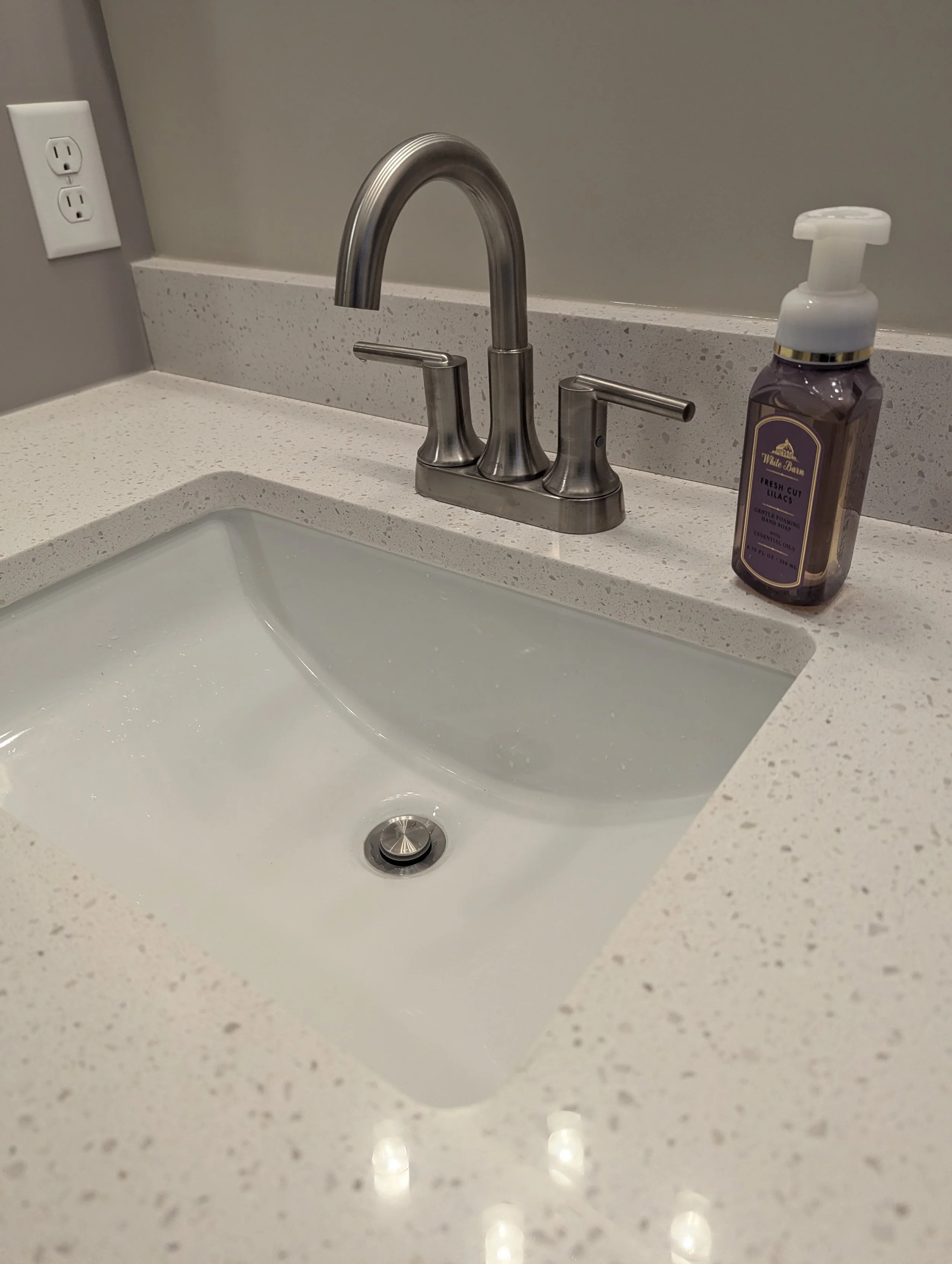 Bathroom sink with a stainless steel faucet, a bottle of hand soap, and a beige speckled countertop.