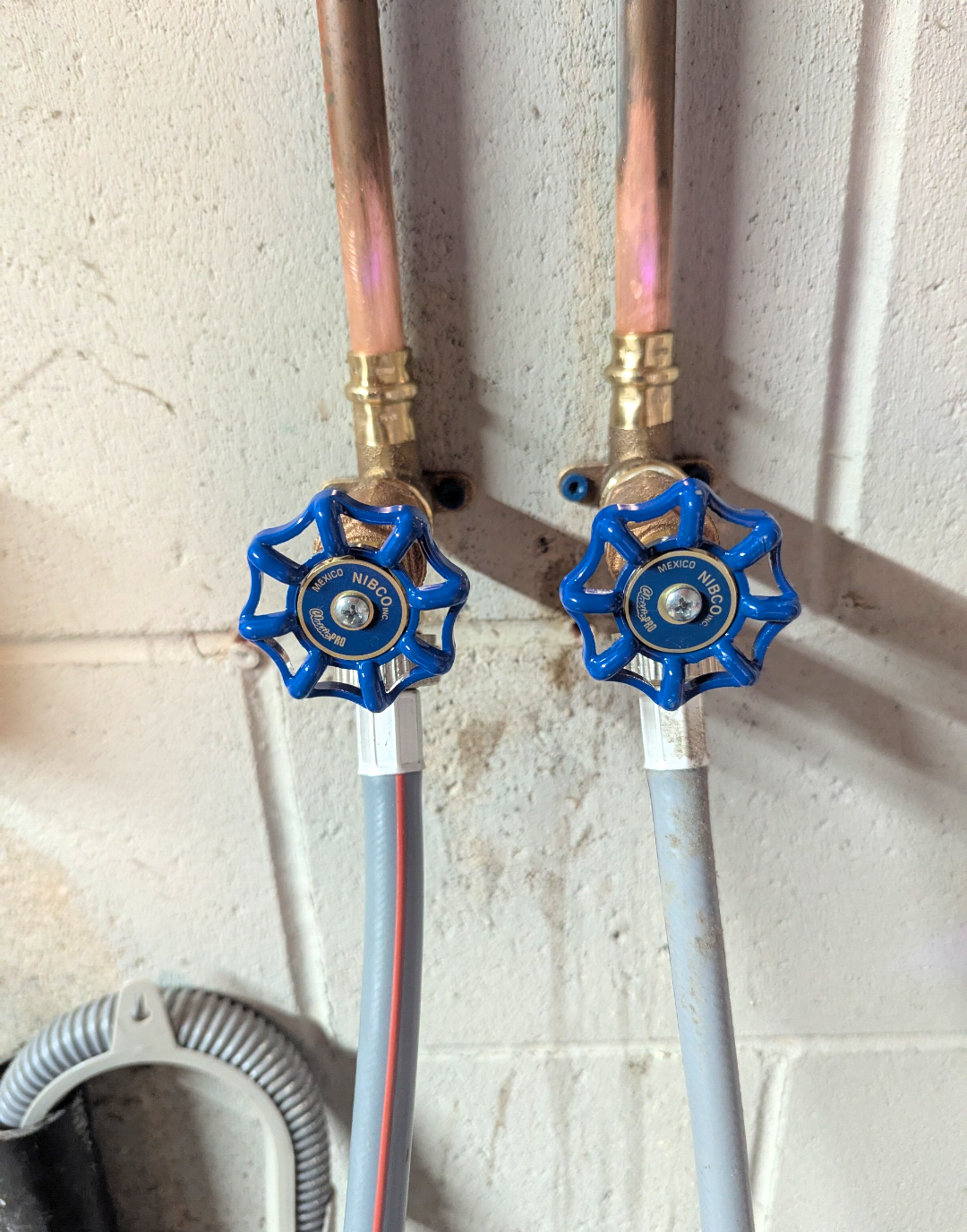 Close-up of two plumbing pipes with blue valve handles labeled 'MEXICO NIBCO' attached to a rough wall.