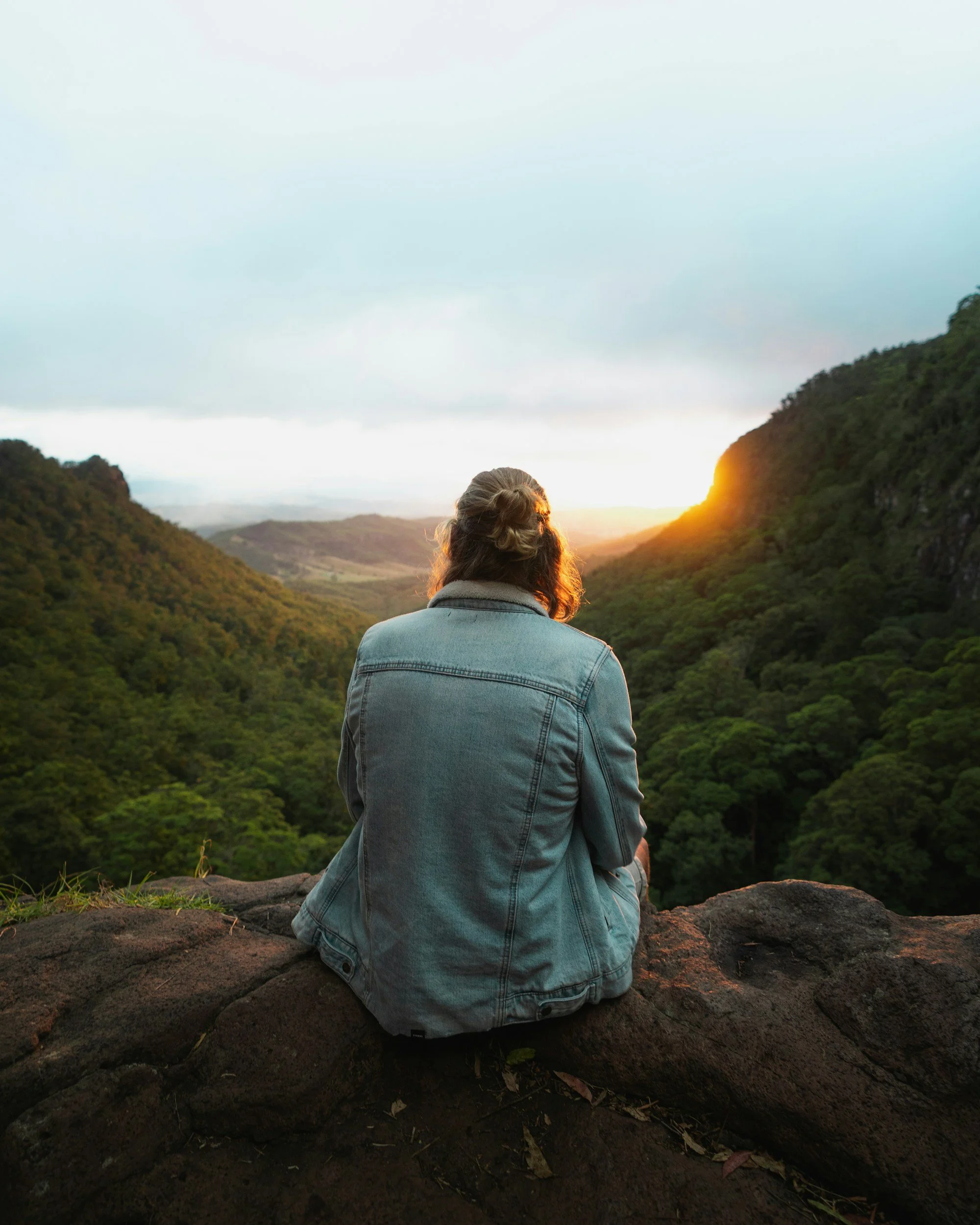 Person sitting on a rock overlooking lush green valley during sunset