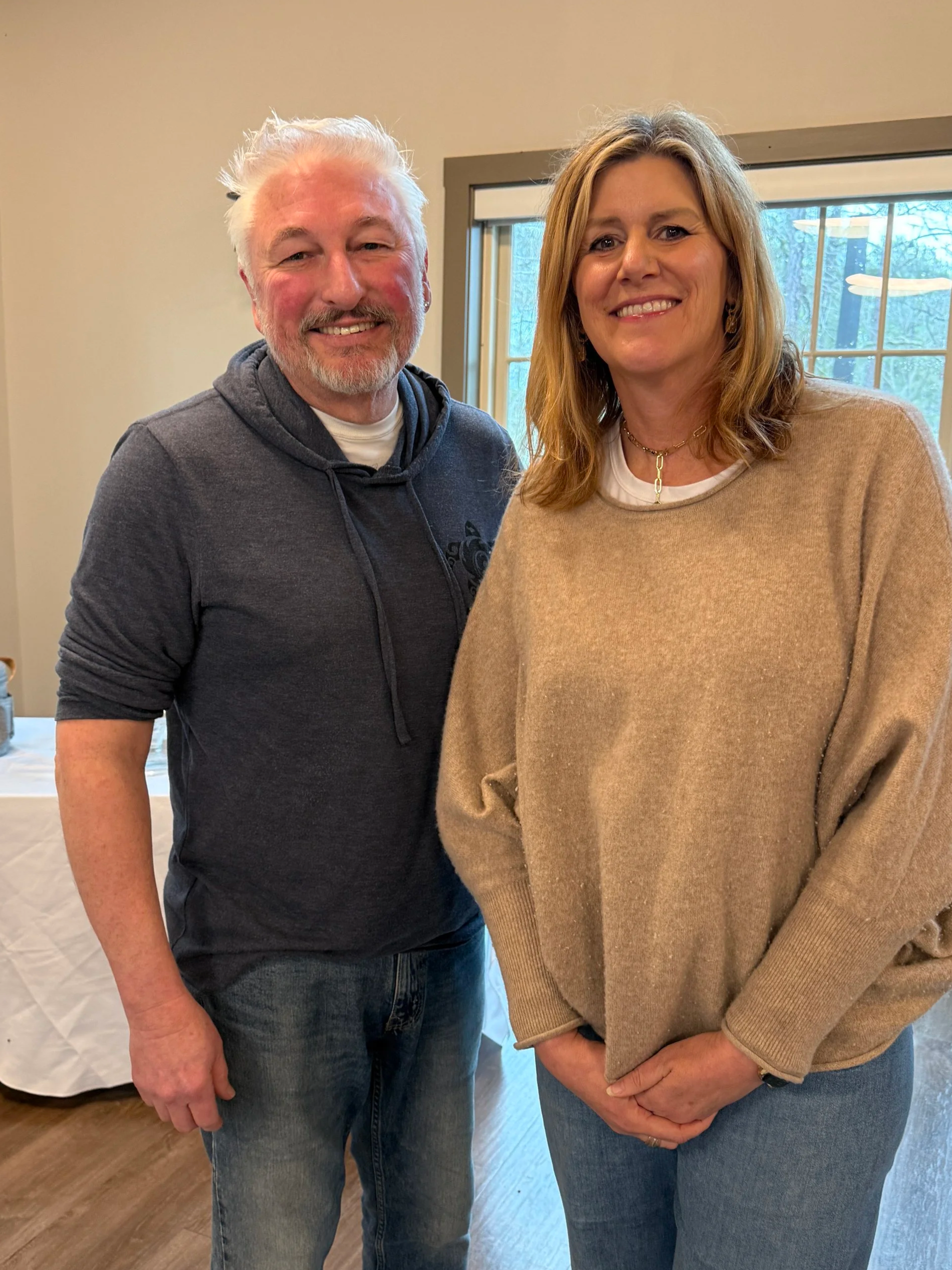 A man and a woman standing indoors, smiling at the camera.