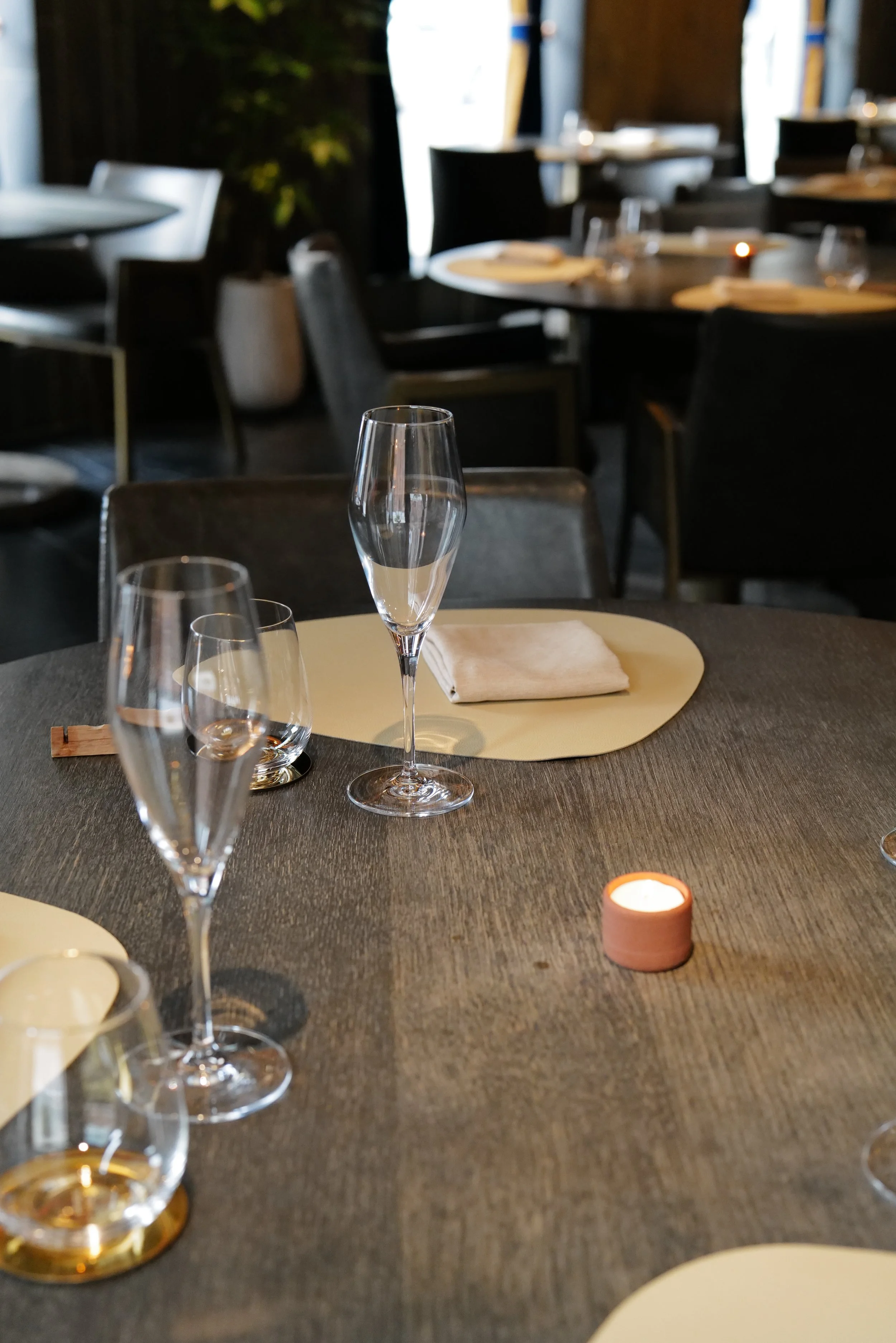 A restaurant table set with empty champagne flutes, a candle, and napkins.