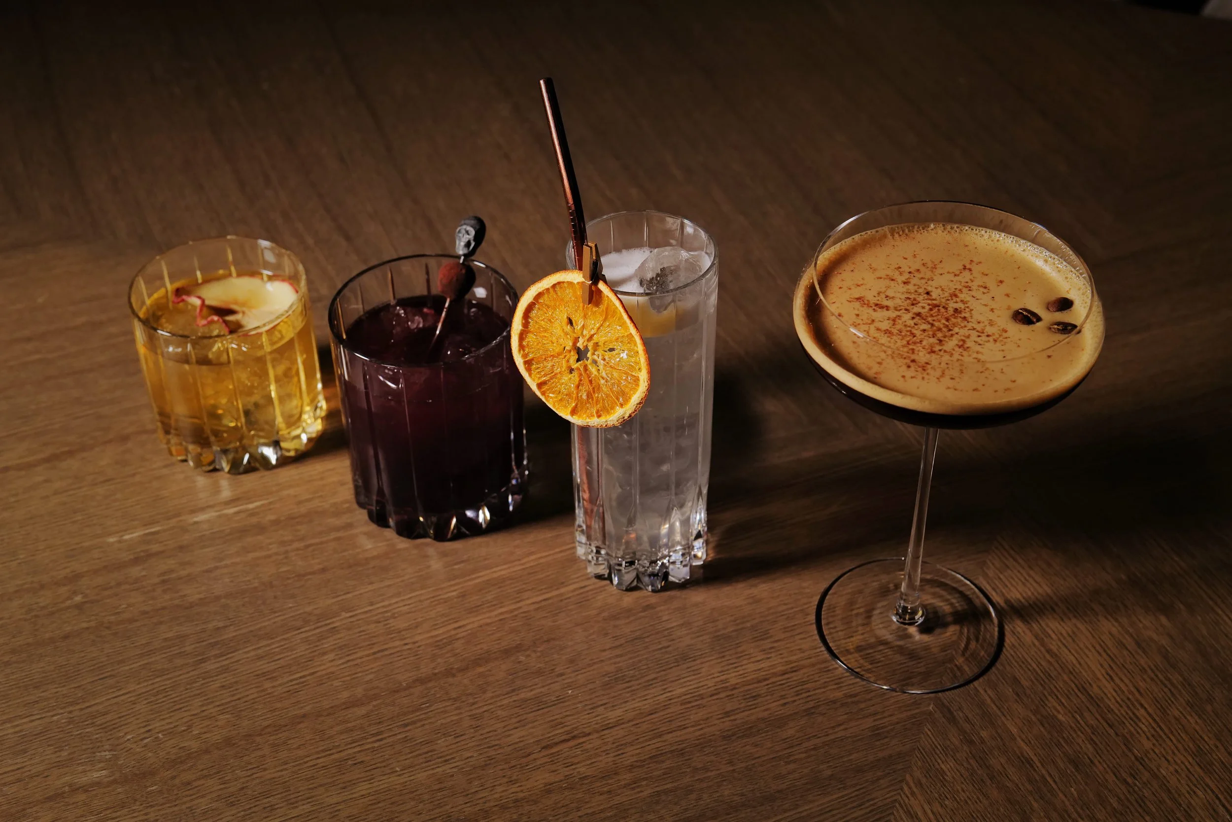 Five different cocktails on a wooden surface, each with distinct colors and garnishes.