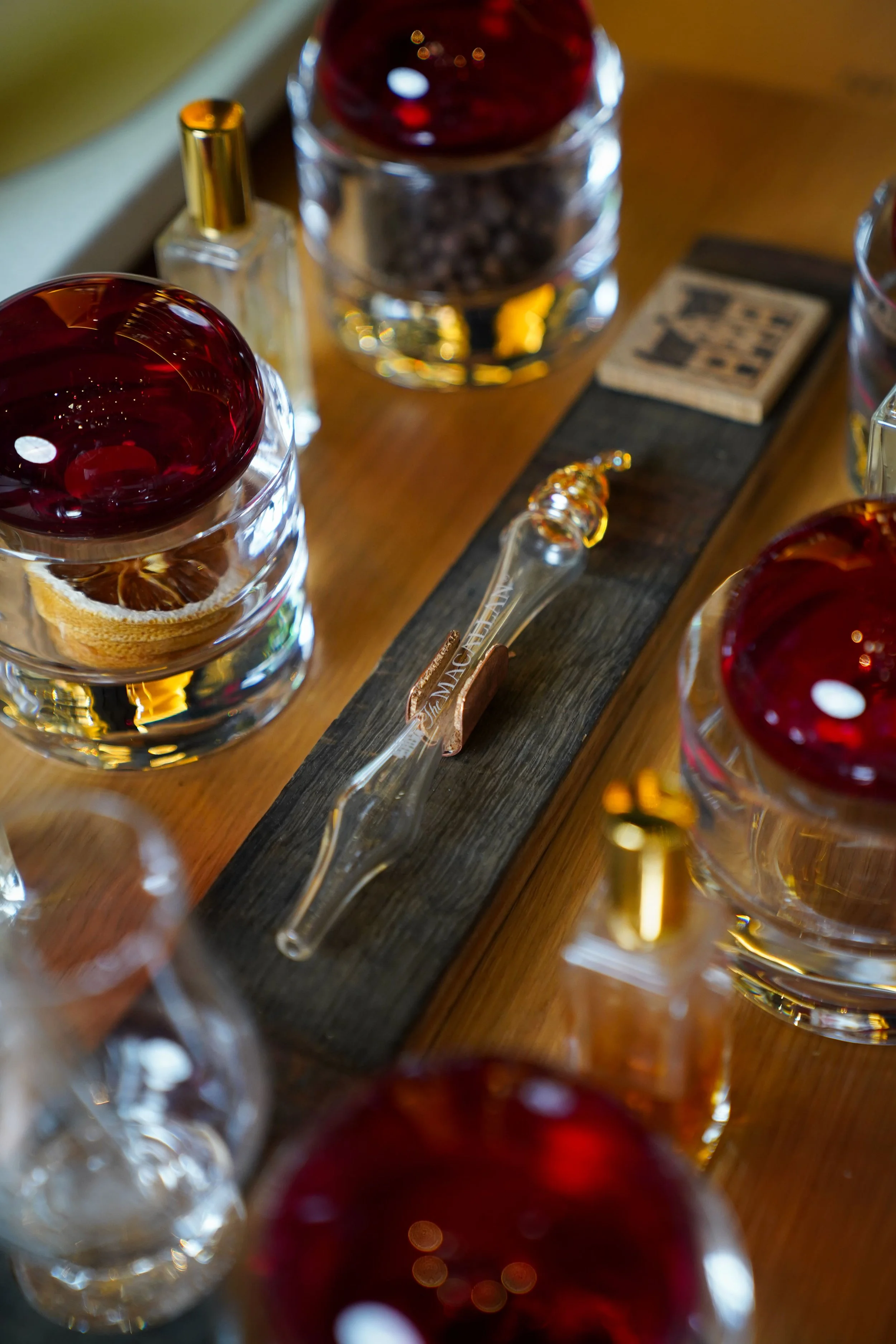 A wooden table displaying bottles of whiskey, glasses with red liquid, and a glass pipette with the word 'MACALLAN' on it.