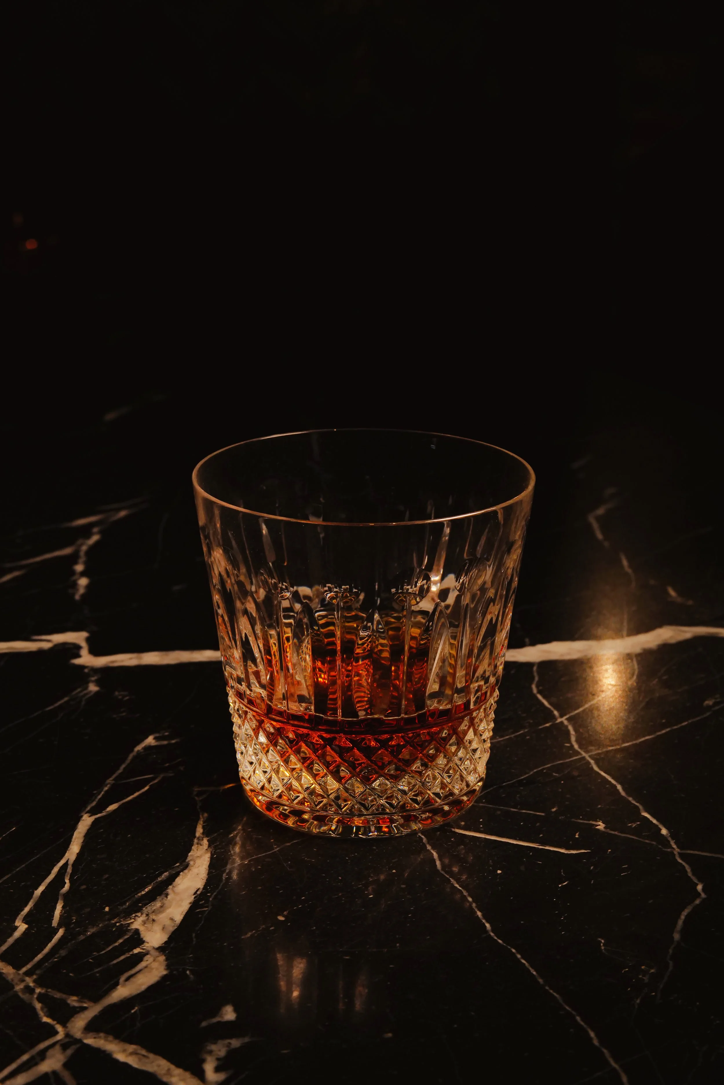 A glass of whiskey on a dark marble surface with a reflective glaze.
