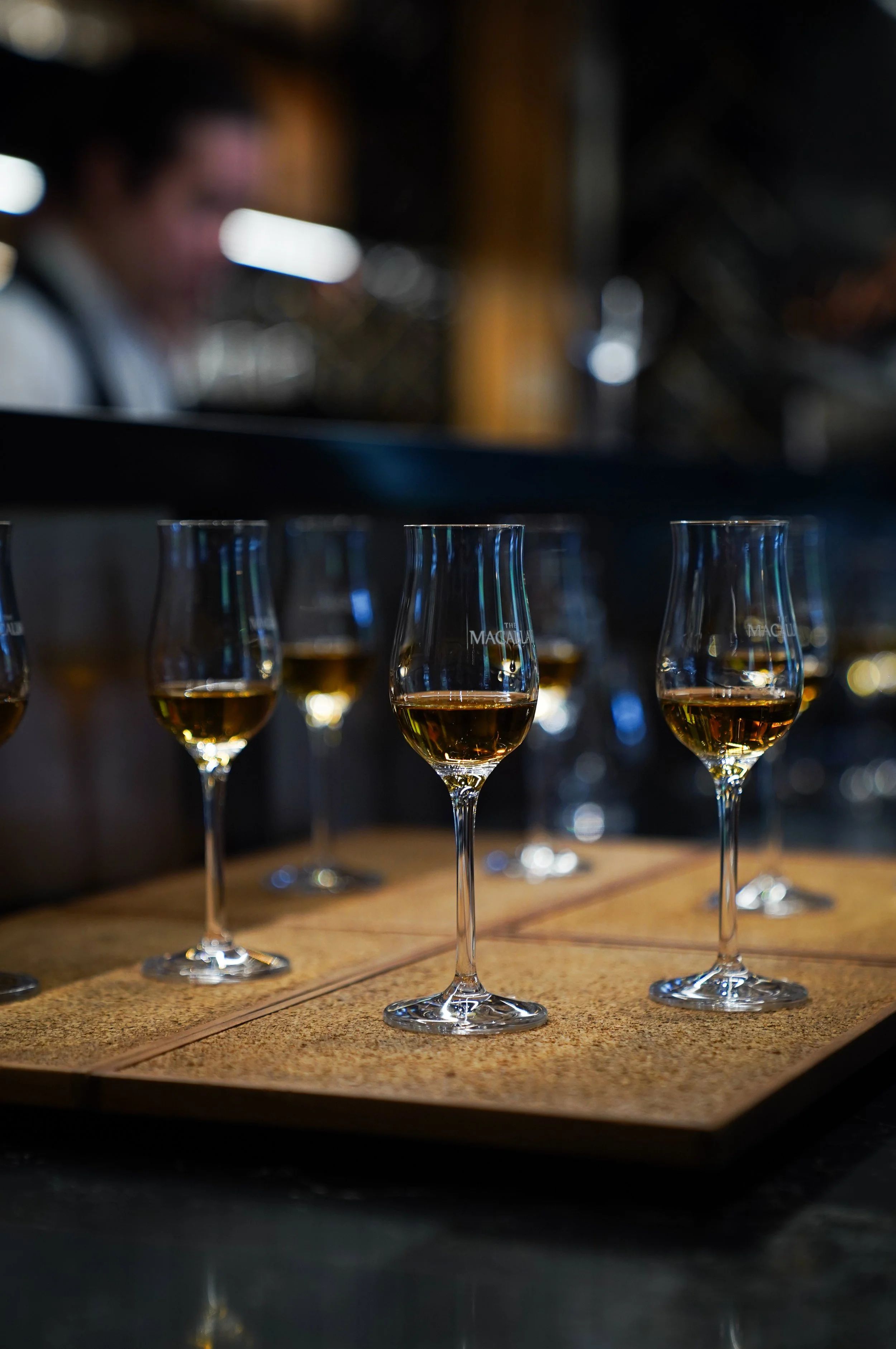 Several glasses of whisky on a wooden tasting board in a dimly lit bar