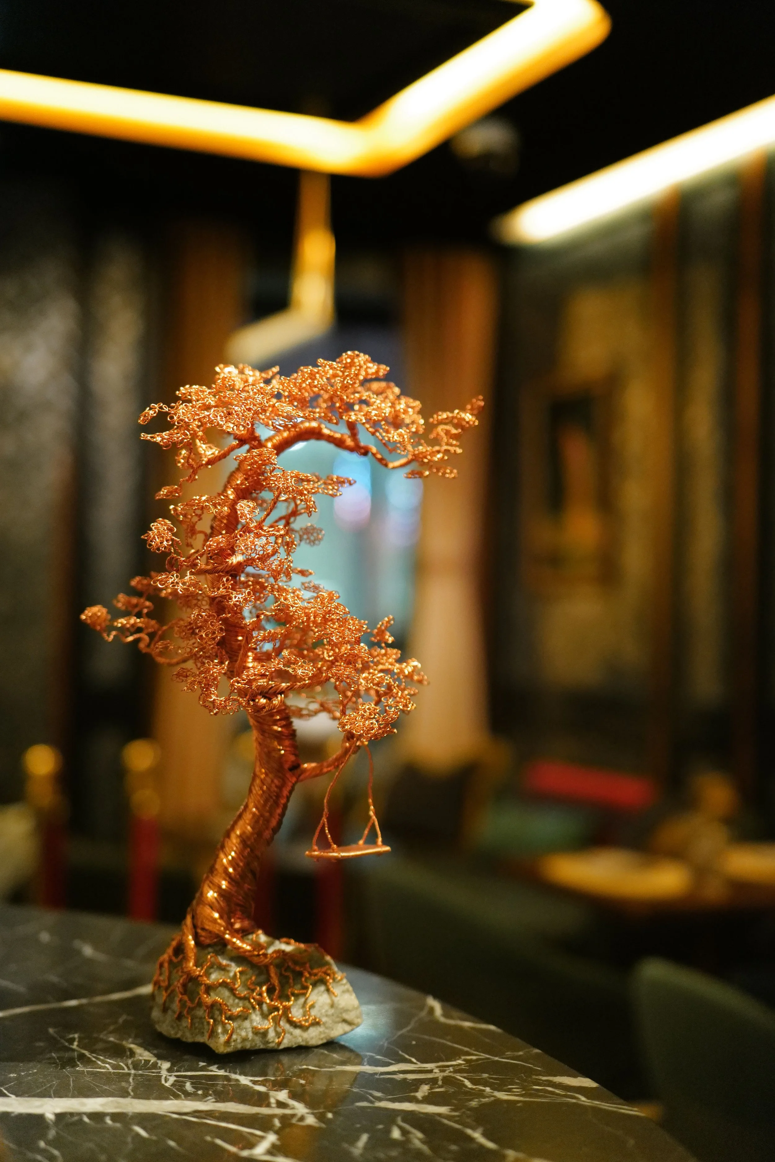 A small decorative copper wire tree sculpture placed on a black marble surface in a sophisticated indoor setting.