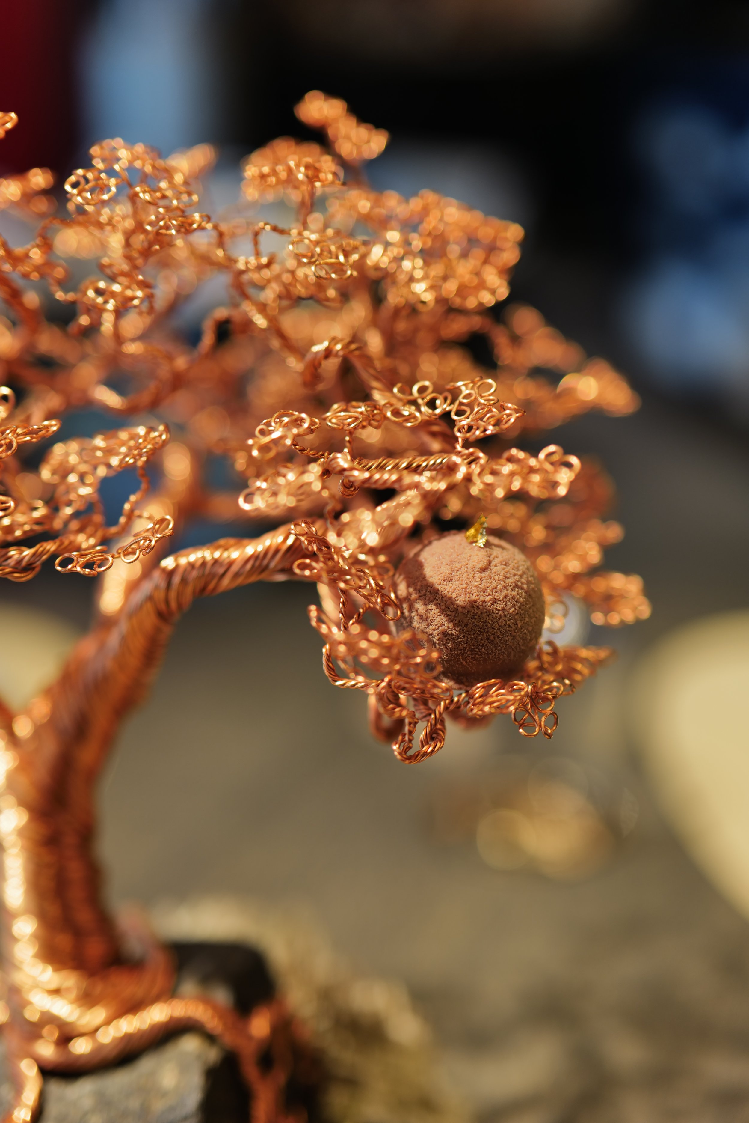 Close-up of a decorative wire tree with copper-colored branches and a fuzzy brown sphere as leaves or fruit.