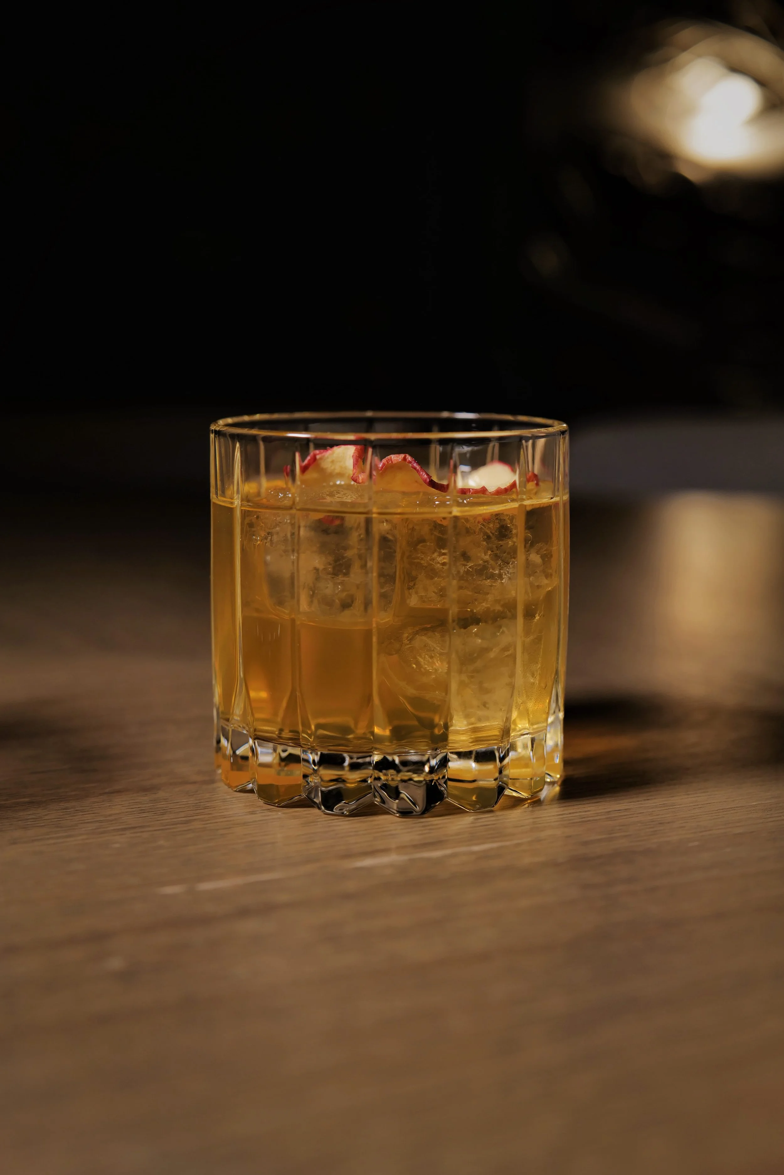 A glass of whiskey with ice and a lemon twist garnish on a wooden surface.