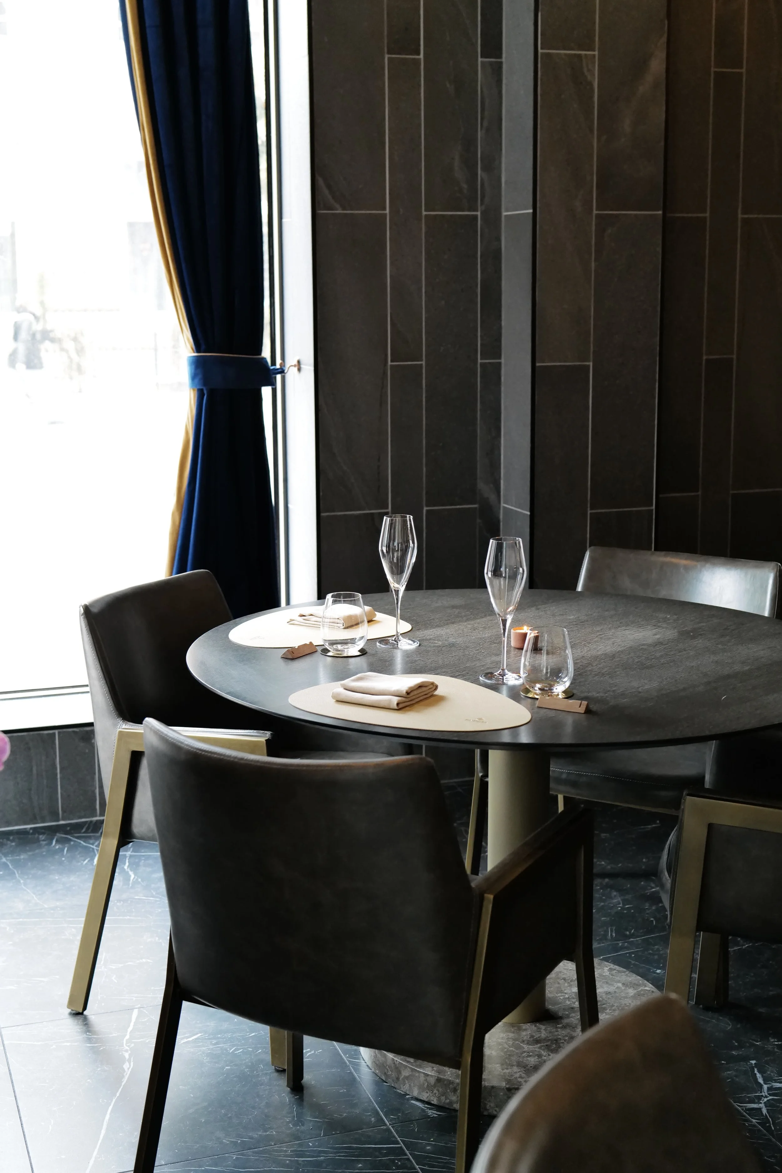 Empty table set with napkins and glasses near a window with blue curtains in a modern dining room.