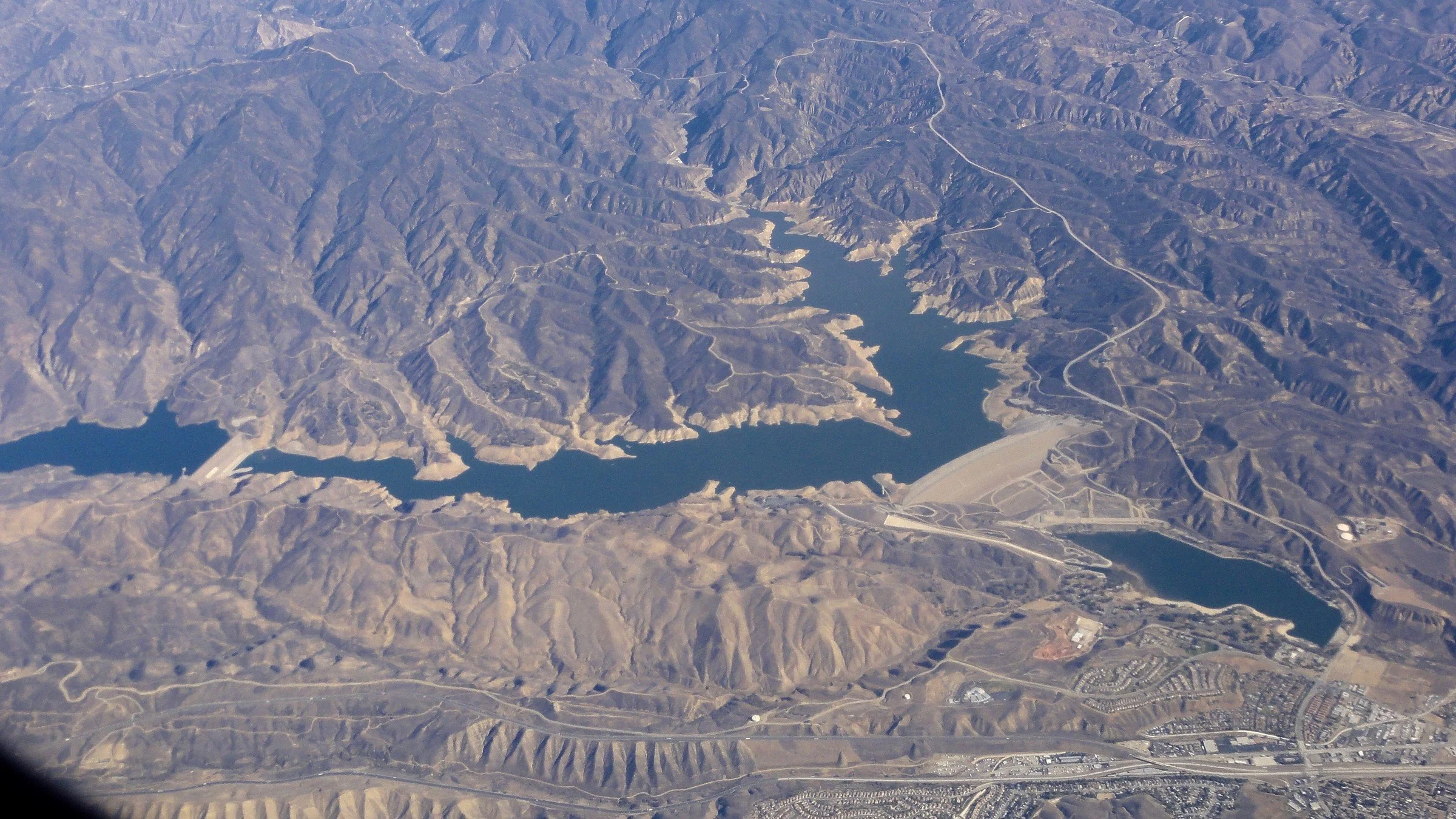 Aerial view of a mountainous landscape with two large reservoirs, surrounded by roads and scattered buildings.