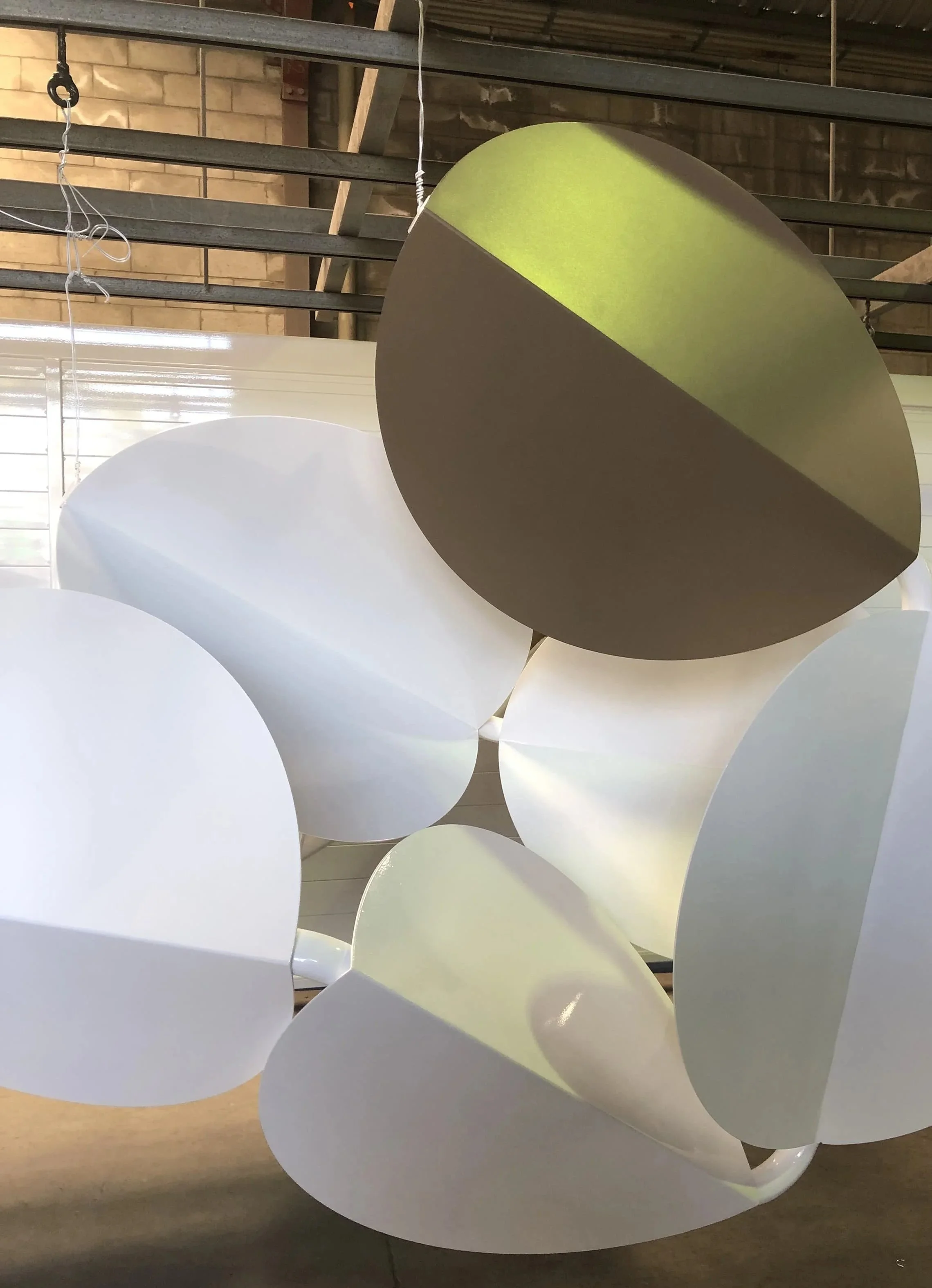 Multiple white and one gold abstract discs, in an industrial-style space with exposed brick walls and metal beams.