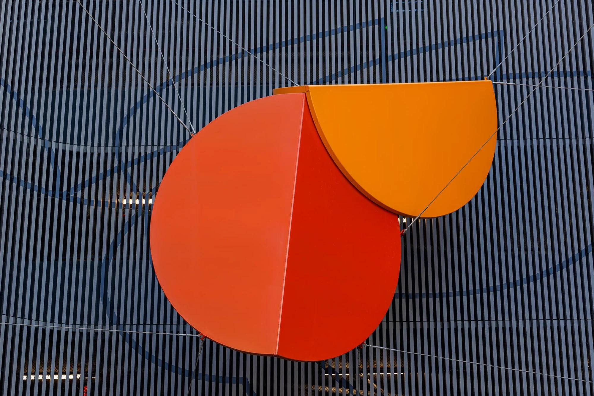 Close-up of a large apple-shaped logo with an orange top and red bottom, mounted on a dark, striped background.