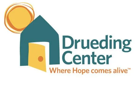 Logo for Drueding Center featuring a stylized house with a yellow door and a sun, along with the slogan "Where Hope comes alive."