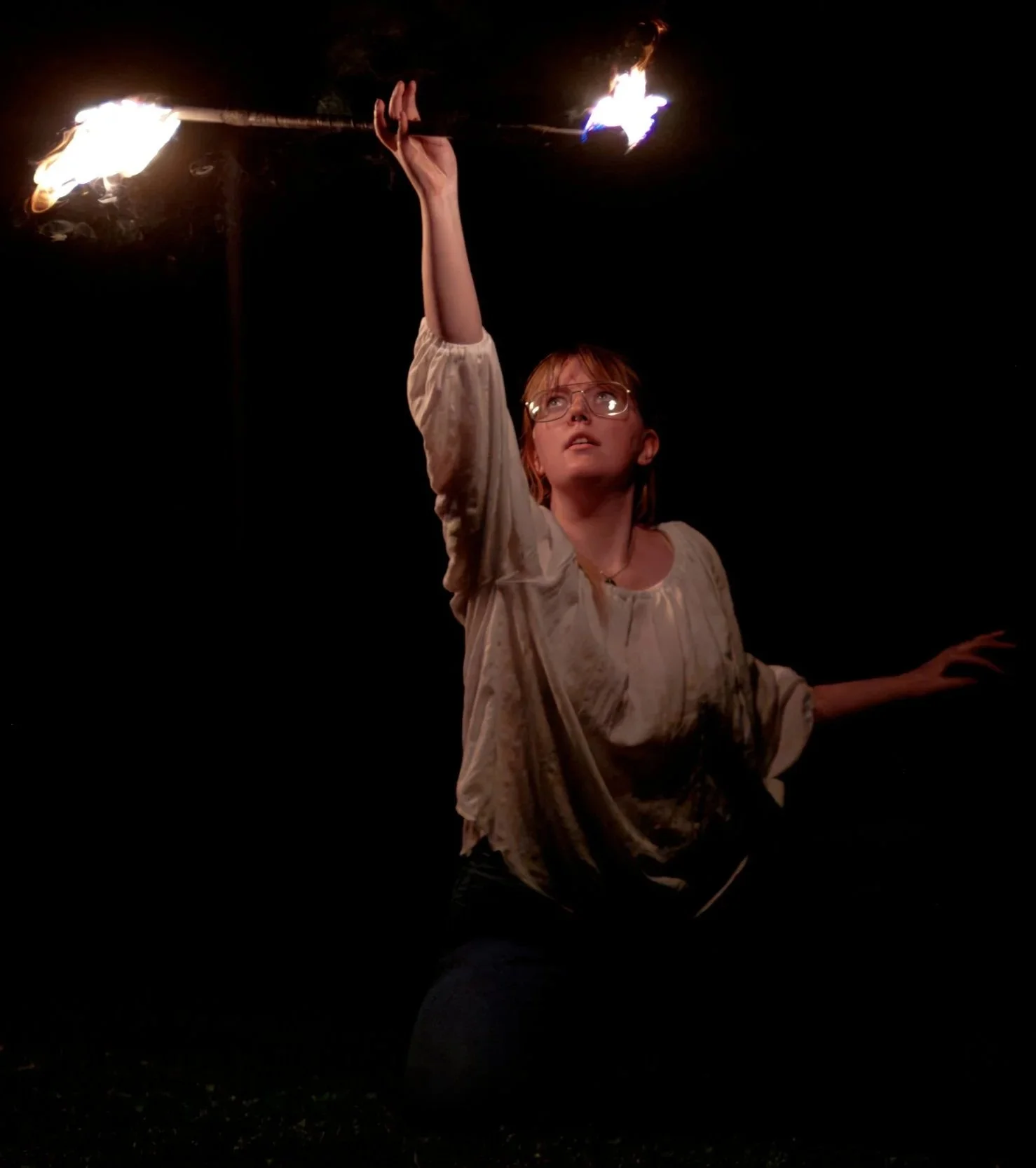 A woman holding a lit flaming torch in the dark.