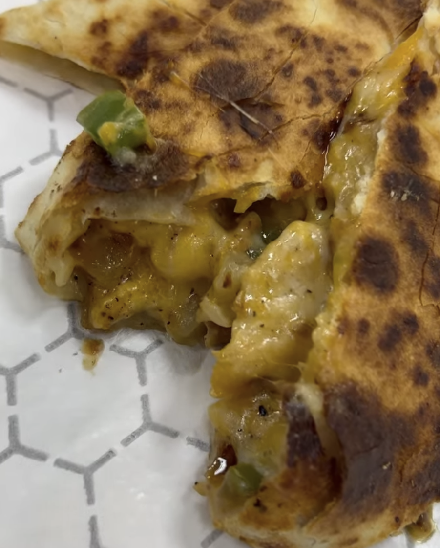 Close-up of a slice of quesadilla with melted cheese and green peppers on a white plate with a geometric pattern.