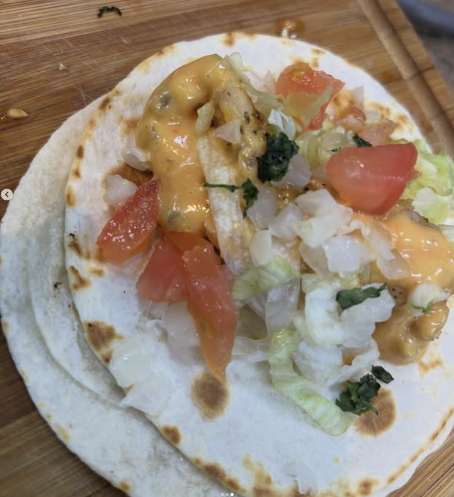 Taco with chopped tomatoes, shredded lettuce, diced onions, green herbs, and cheese on a soft flour tortilla.