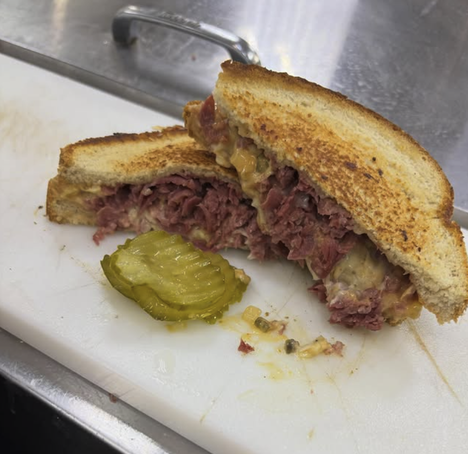 Half of a meatloaf sandwich on toasted bread with pickles on white cutting board.