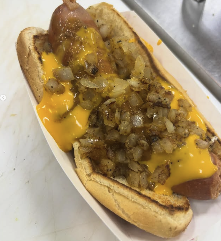 Hot dog in a bun topped with melted cheddar cheese and fried diced onions.