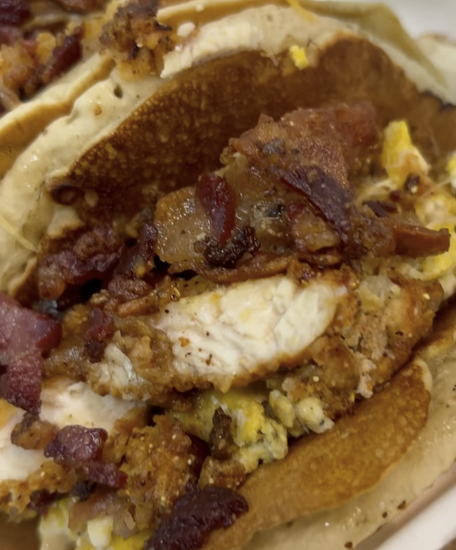 Close-up of a breakfast taco with scrambled eggs, bacon, and sausage in a tortilla.