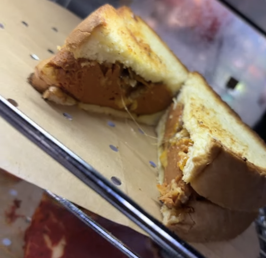 Close-up of a grilled cheese sandwich with melted cheese and a slice of tomato, cut in half and served on a metal tray.