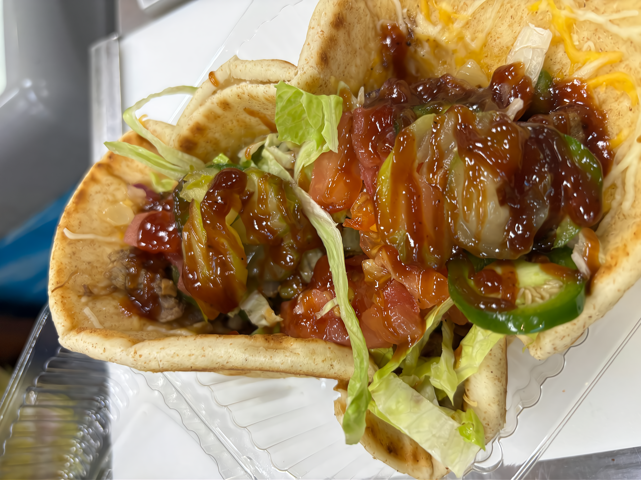 Two tacos with lettuce, tomatoes, jalapeños, shredded cheese, and salsa in soft corn tortillas.