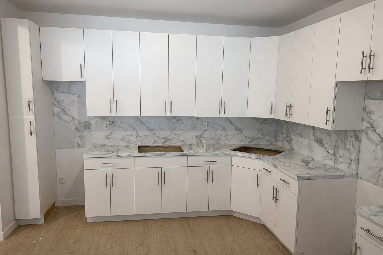 Empty white kitchen cabinets with marble countertops and backsplash, under construction with openings for appliances, on hardwood floor.