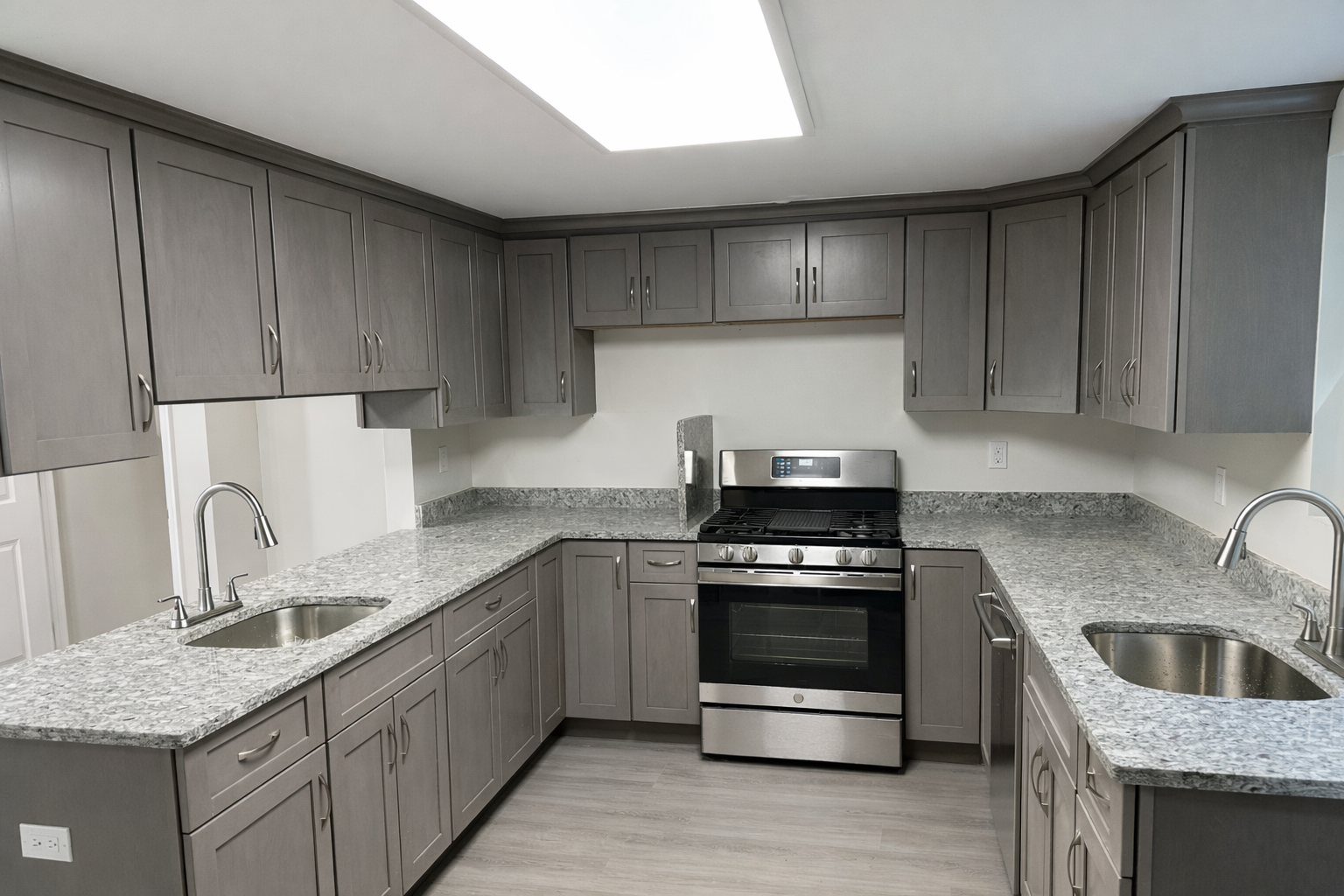 Modern kitchen with gray cabinets, granite countertops, stainless steel oven, and two sinks.