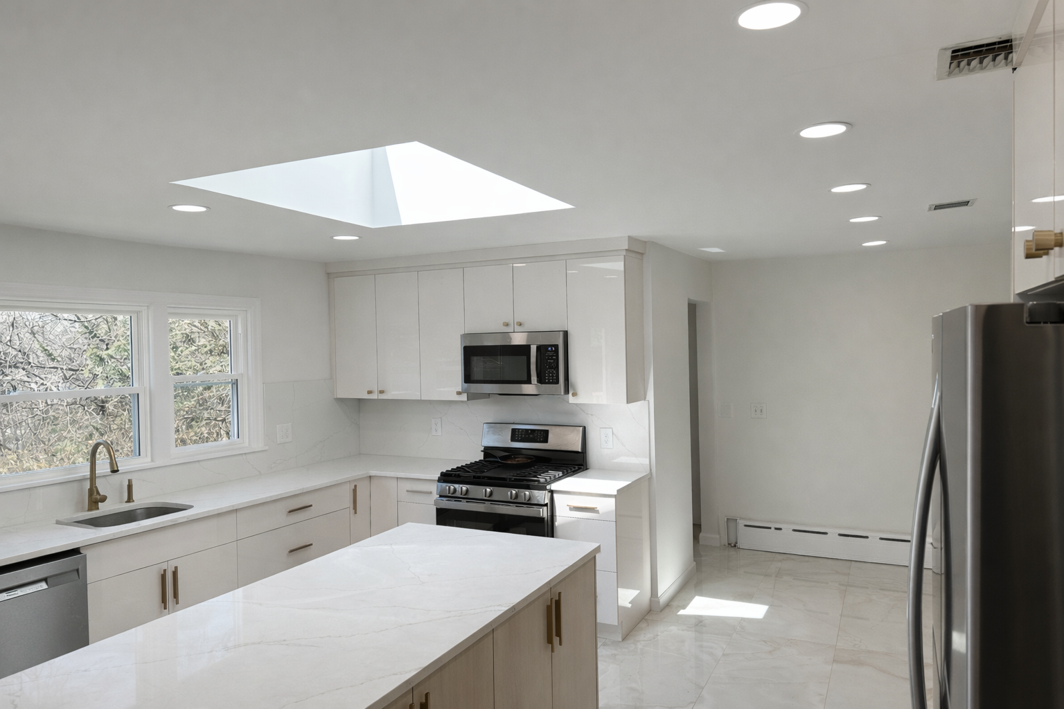 Modern white kitchen with skylight, marble countertops, stainless steel appliances, and two double-hung windows.