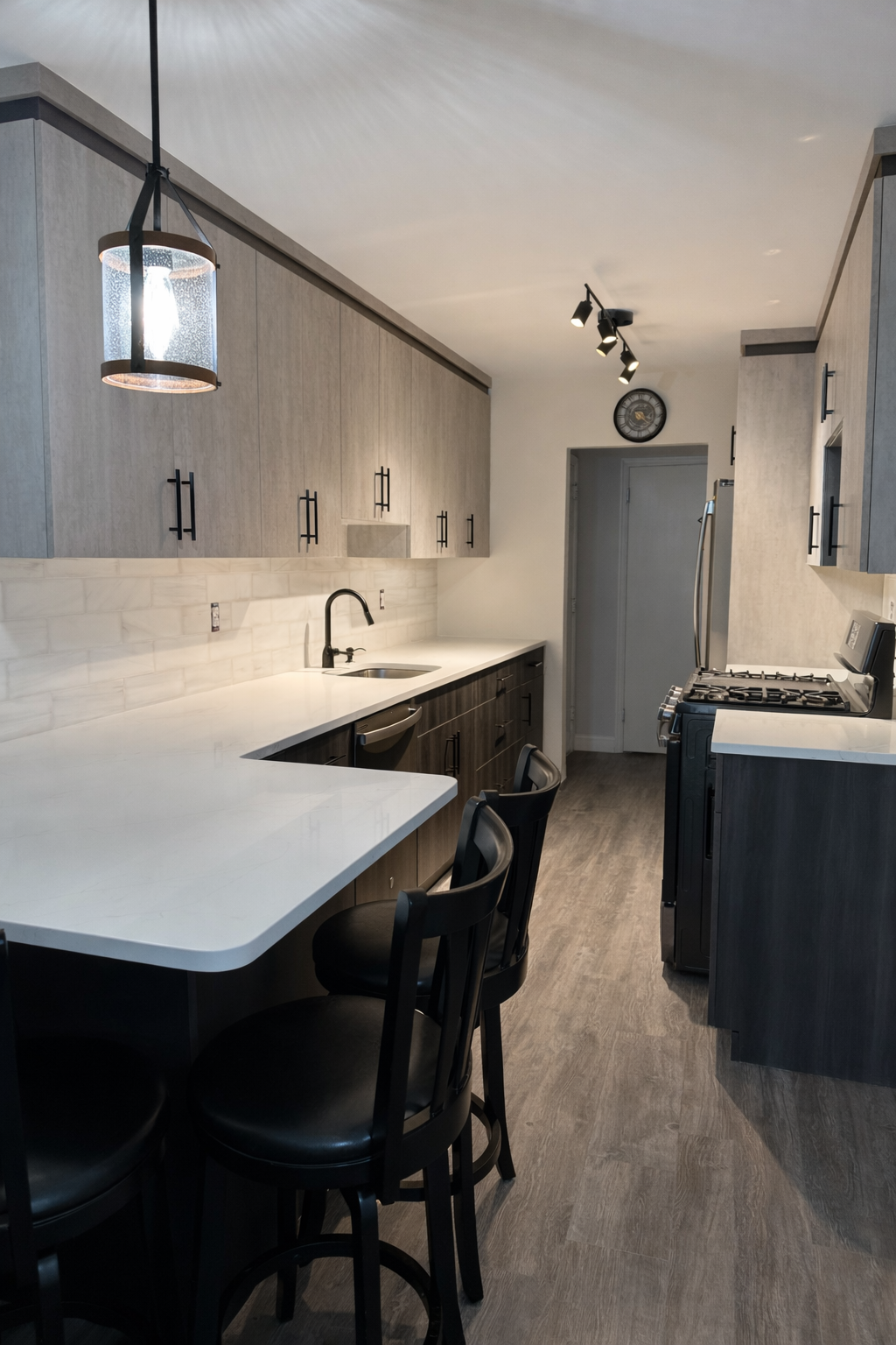 Modern kitchen with gray cabinets, white countertop, black hardware, a black faucet, and a small island with three black chairs. Includes a stove, dishwasher, and a clock on the wall.