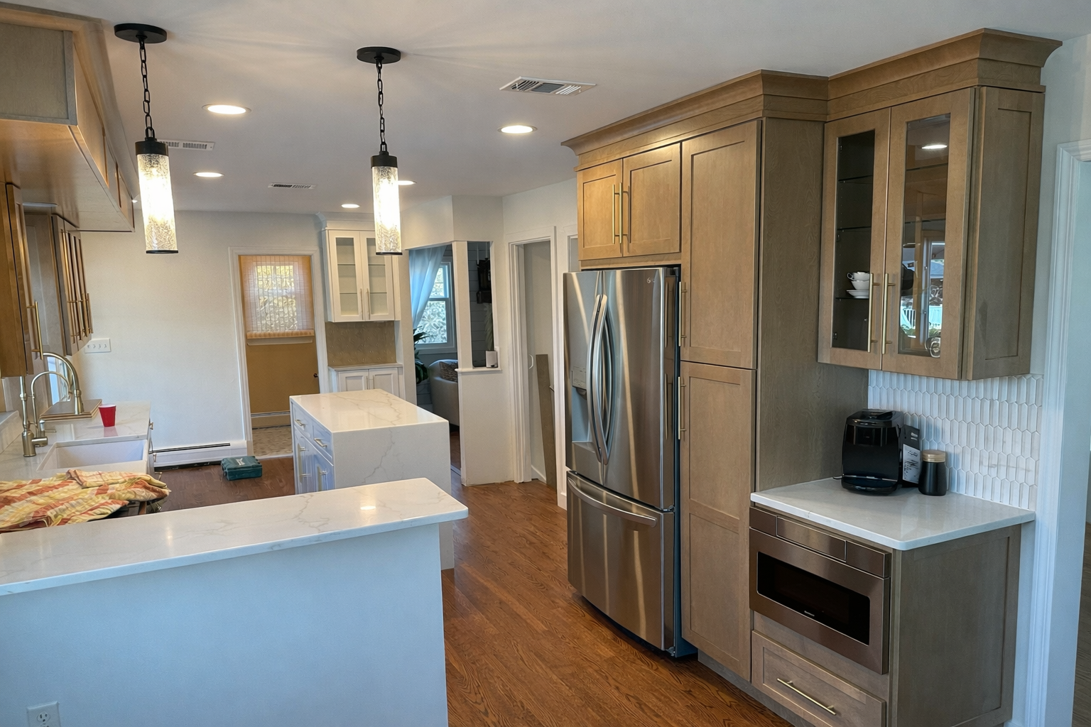 Kitchen with wooden cabinets, stainless steel refrigerator, white marble countertops, coffee maker, microwave, and pendant lights.