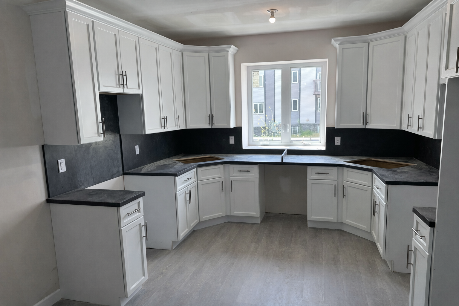 A kitchen with white cabinets, black countertops, a window in the center, and space for appliances.