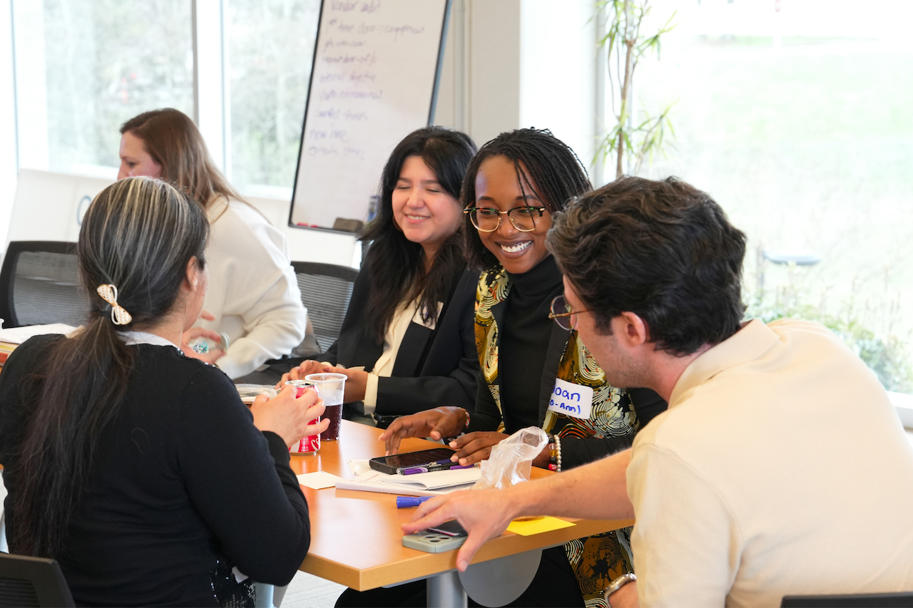 Group of diverse women sitting around a table, smiling and engaging in conversation during a meeting or workshop.