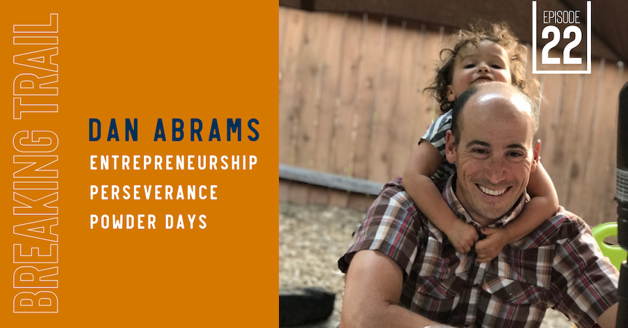 Dan Abrams, founder of FlyLow, with his daughter on his shoulders, smiling outdoors near a wooden fence.