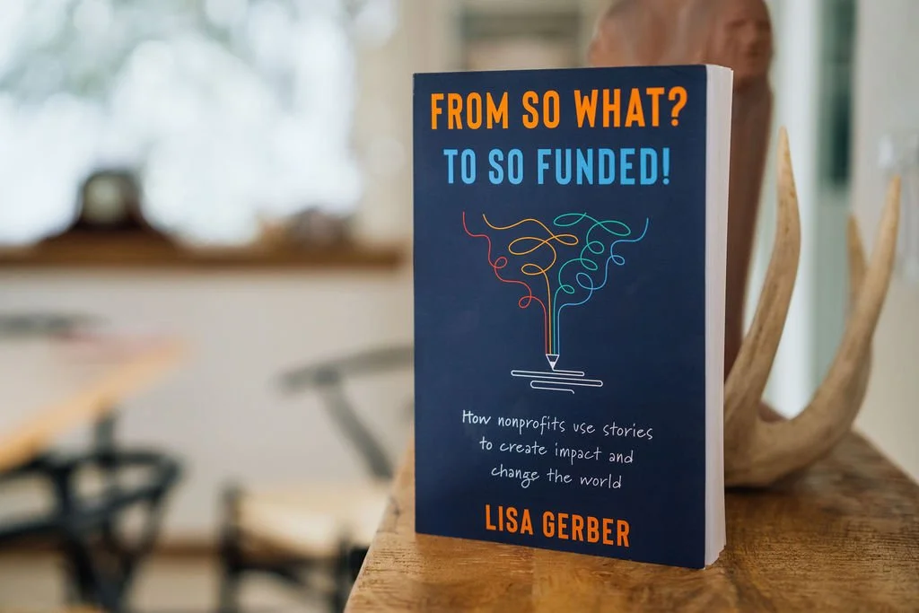 Book titled "From So What? to So Funded!" by Lisa Gerber on a wooden table in a cozy room with blurred background.