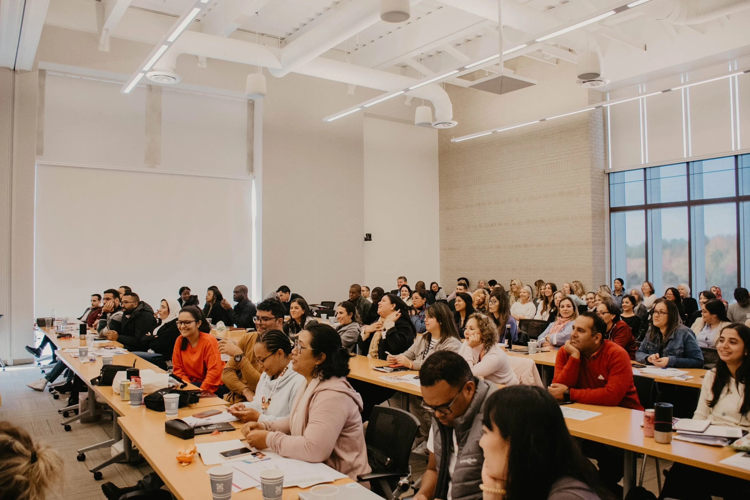 Large group of people attending a conference or seminar conference room with high ceilings, large windows, and modern lighting.