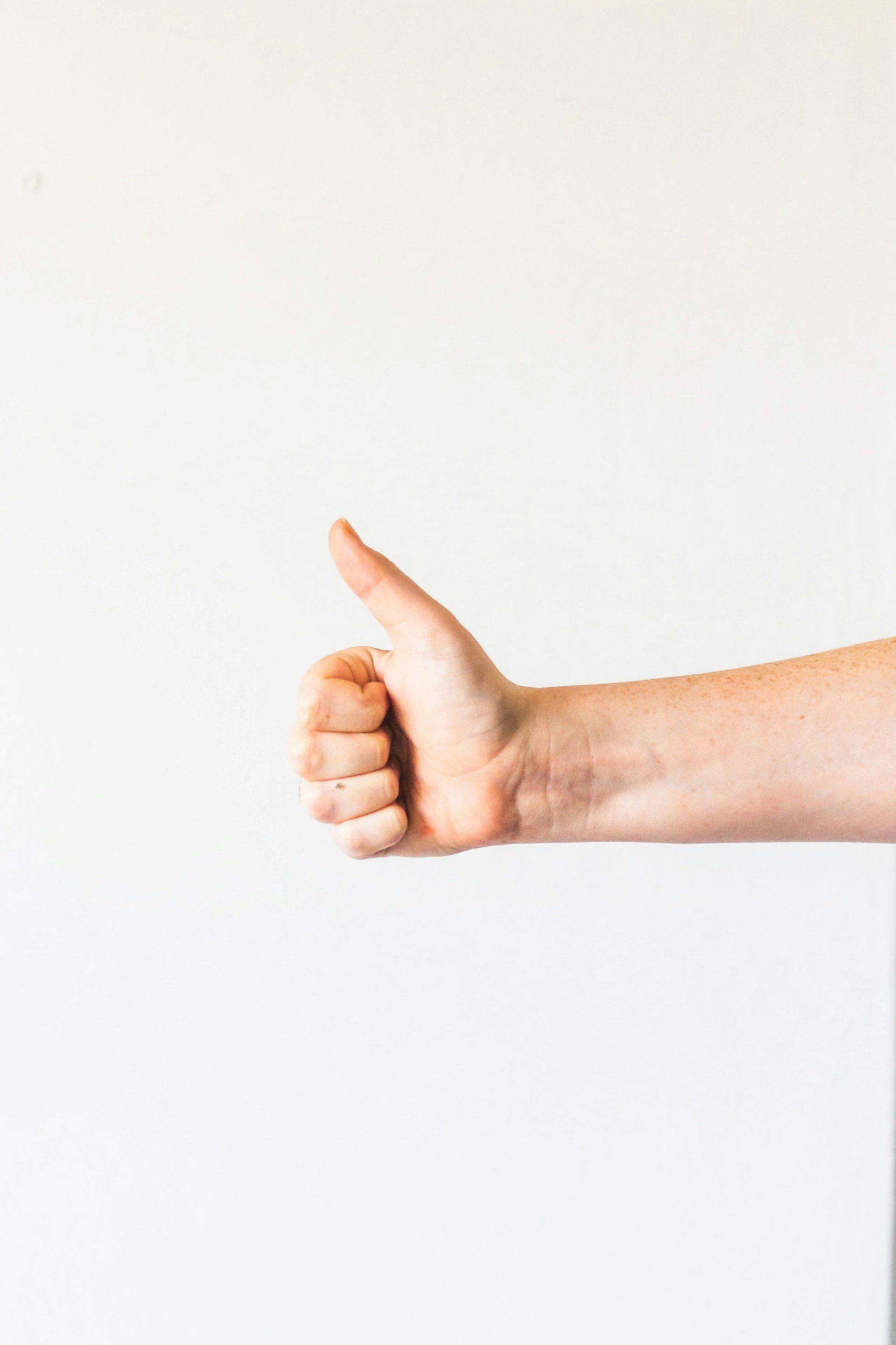 A person's arm extended to the right with their thumb up in a thumbs-up gesture against a white background.