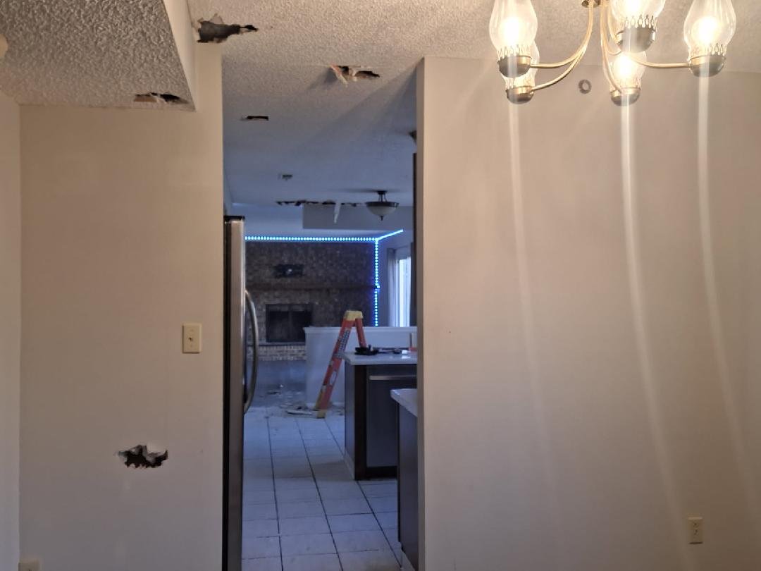 Ceiling with multiple holes and a chandelier in a room with visible construction or damage.