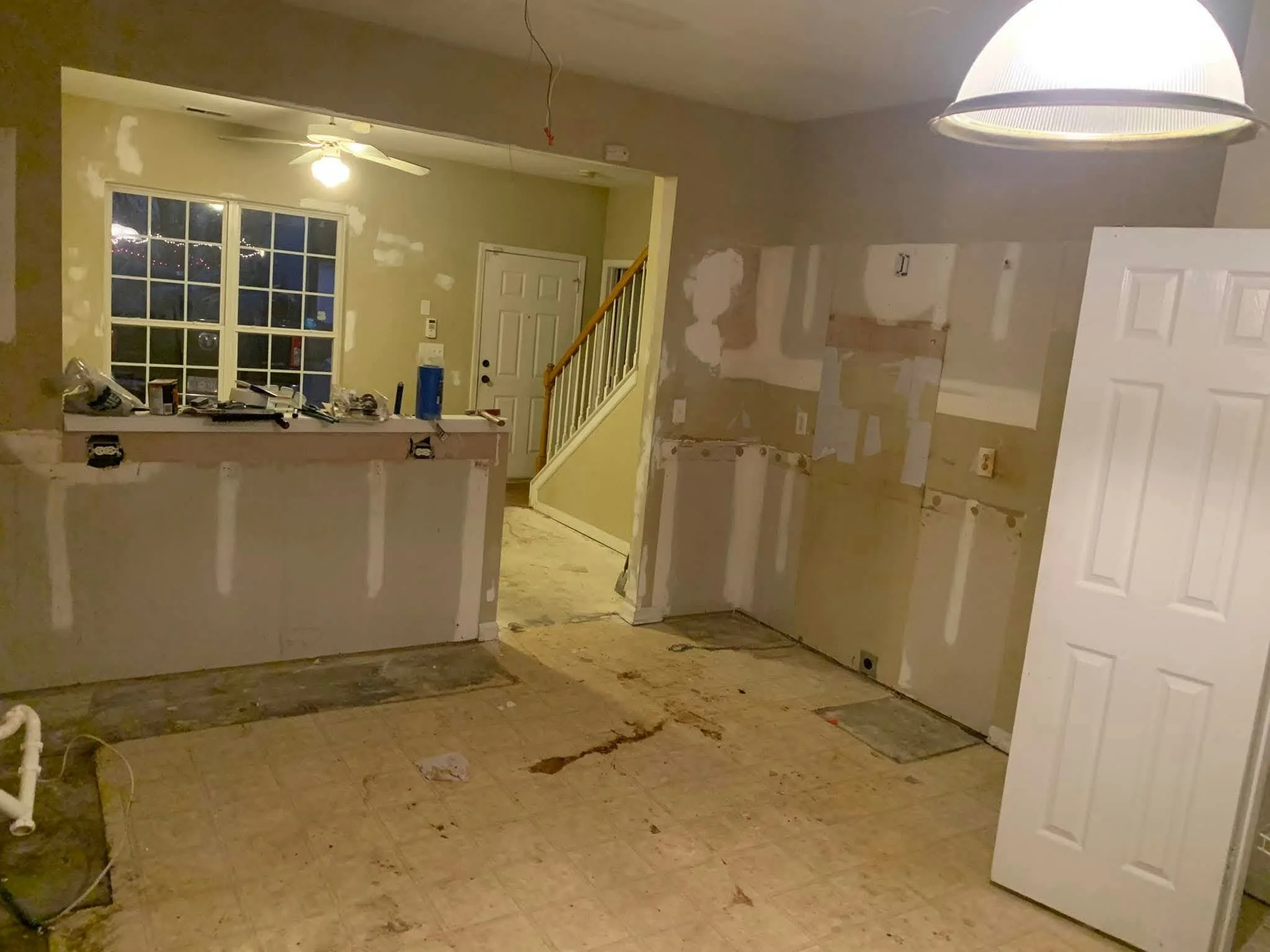A room under renovation with partially removed wall coverings, construction tools and materials on the counter, and unfinished flooring.