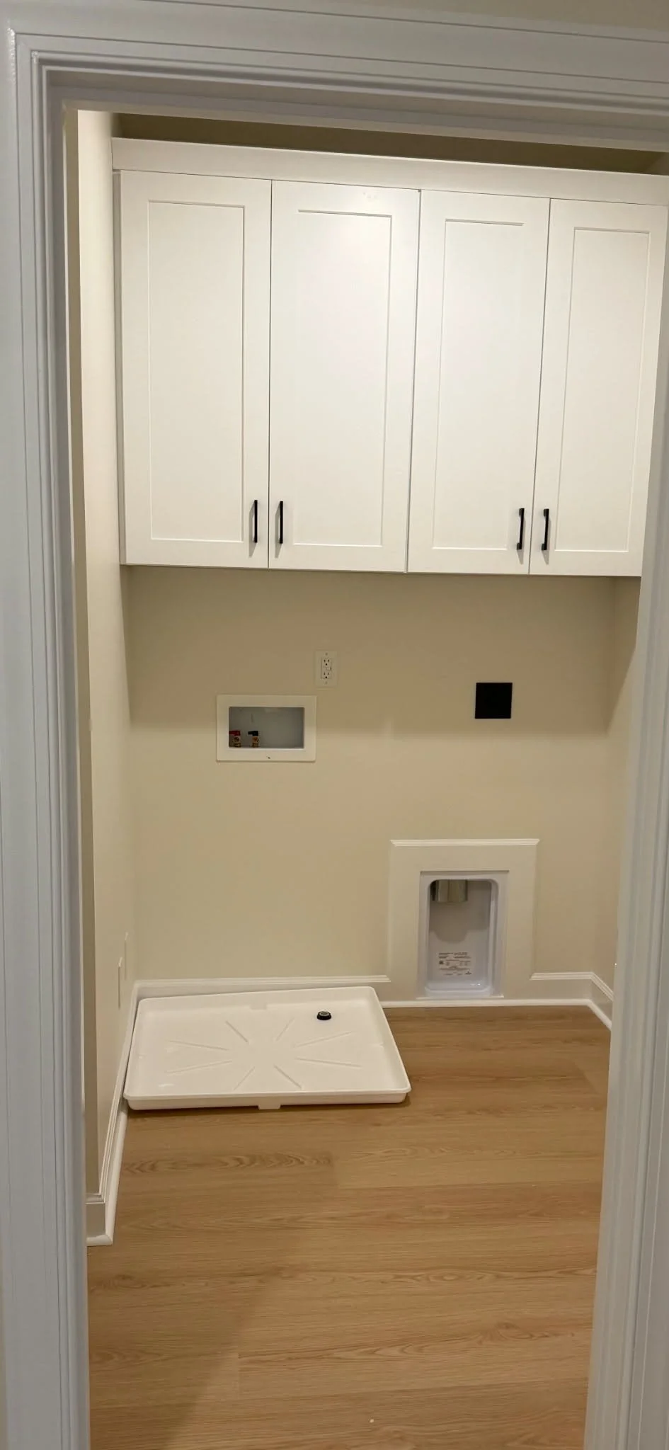 Empty laundry room with white cabinets, a white plastic laundry tray on the wooden floor, and hookups for washer and dryer.