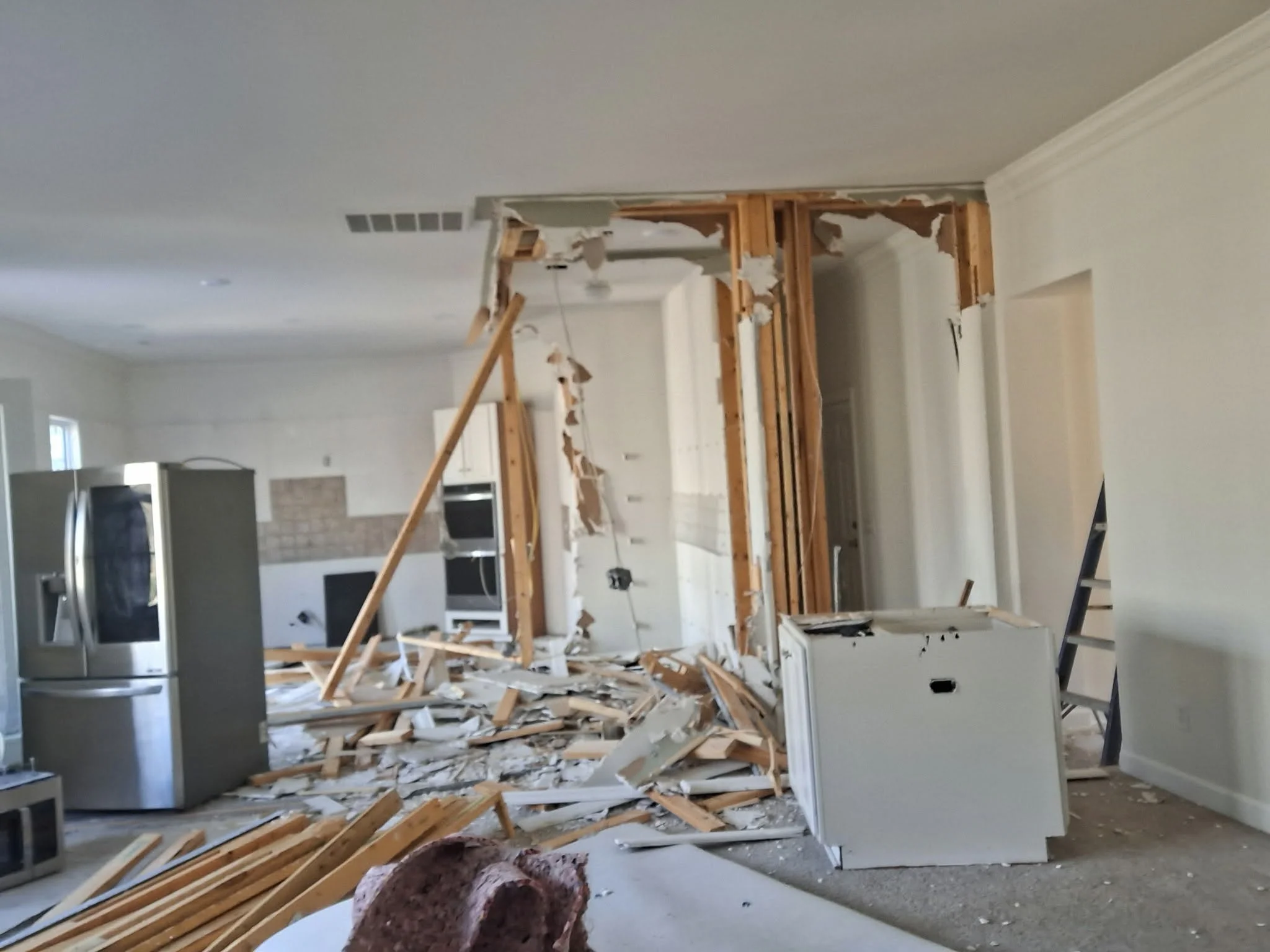Interior of a house under renovation with a partially demolished wall, scattered wooden studs, debris, and construction tools.