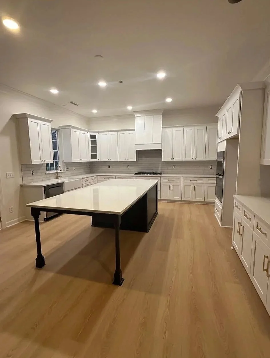 Modern kitchen with white cabinets, wooden flooring, central island, and stainless steel appliances.