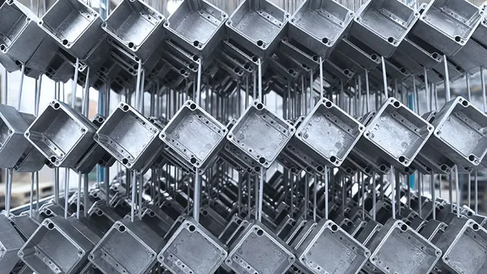 Multiple metal enclosures, possibly electrical boxes, stacked and hanging on metal racks in a manufacturing or warehouse setting.