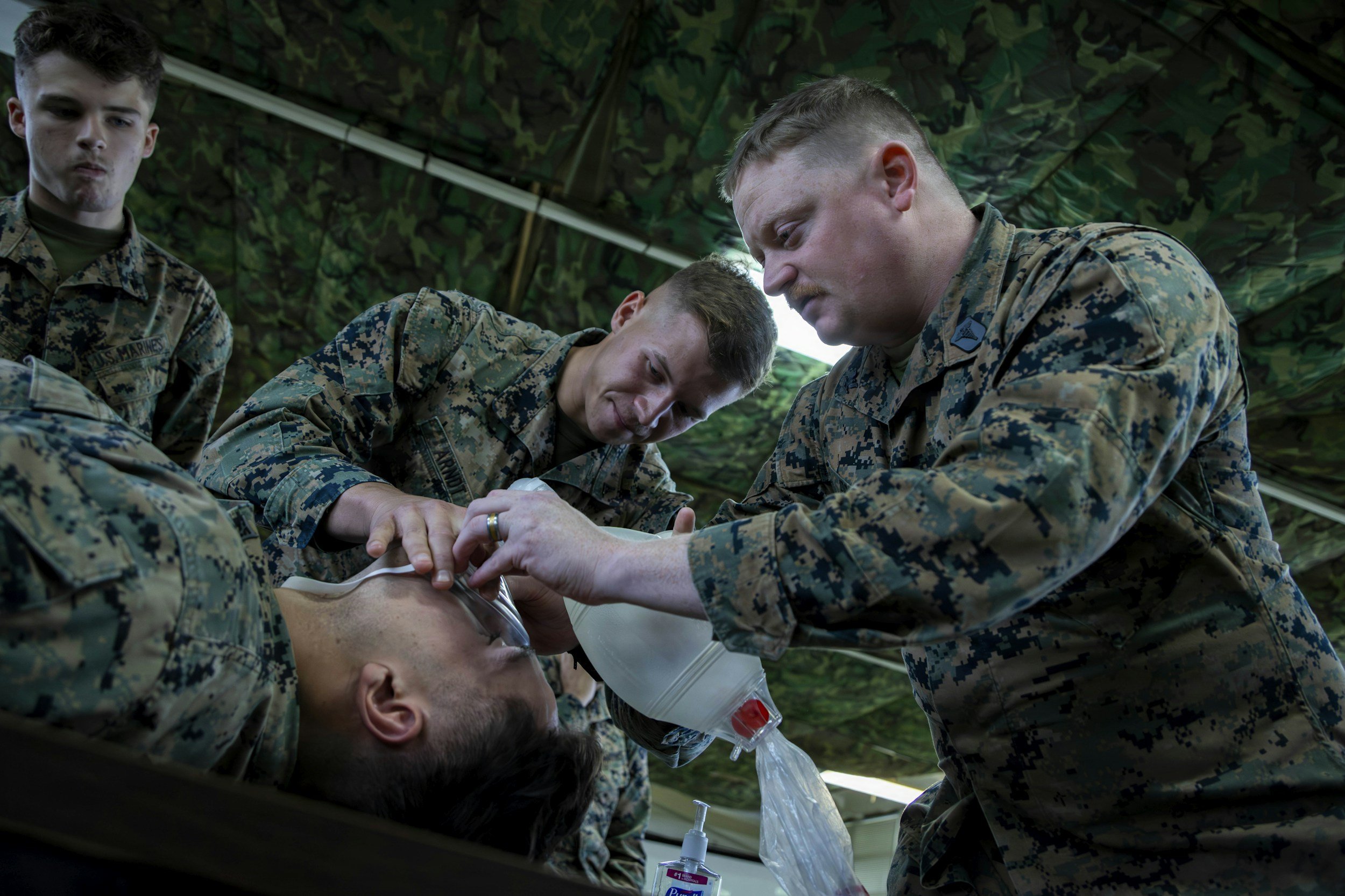 Military personnel administering oxygen to a seated soldier during a training exercise under a camouflage tent. Real-world experience in high stress operations make Strongpoint LLC unique operating partner.