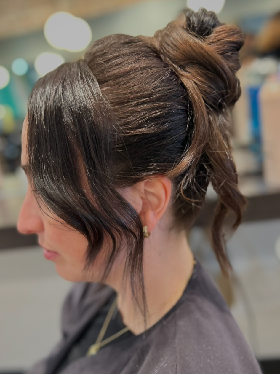 Side view of a woman with dark hair styled in loose waves and an elegant updo, in a salon setting.